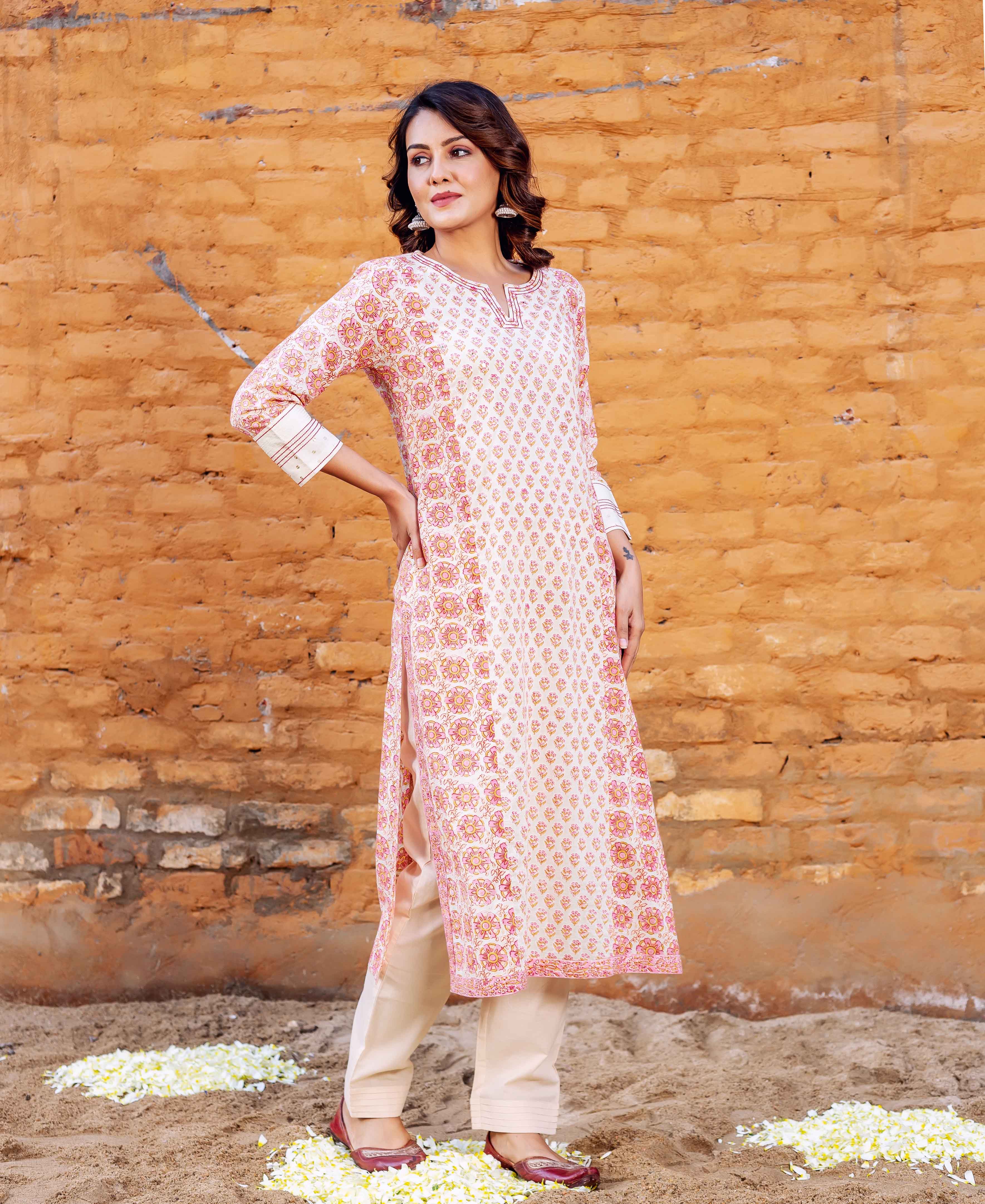 Standing model in white block printed straight kurta with pink motifs and light beige pants.