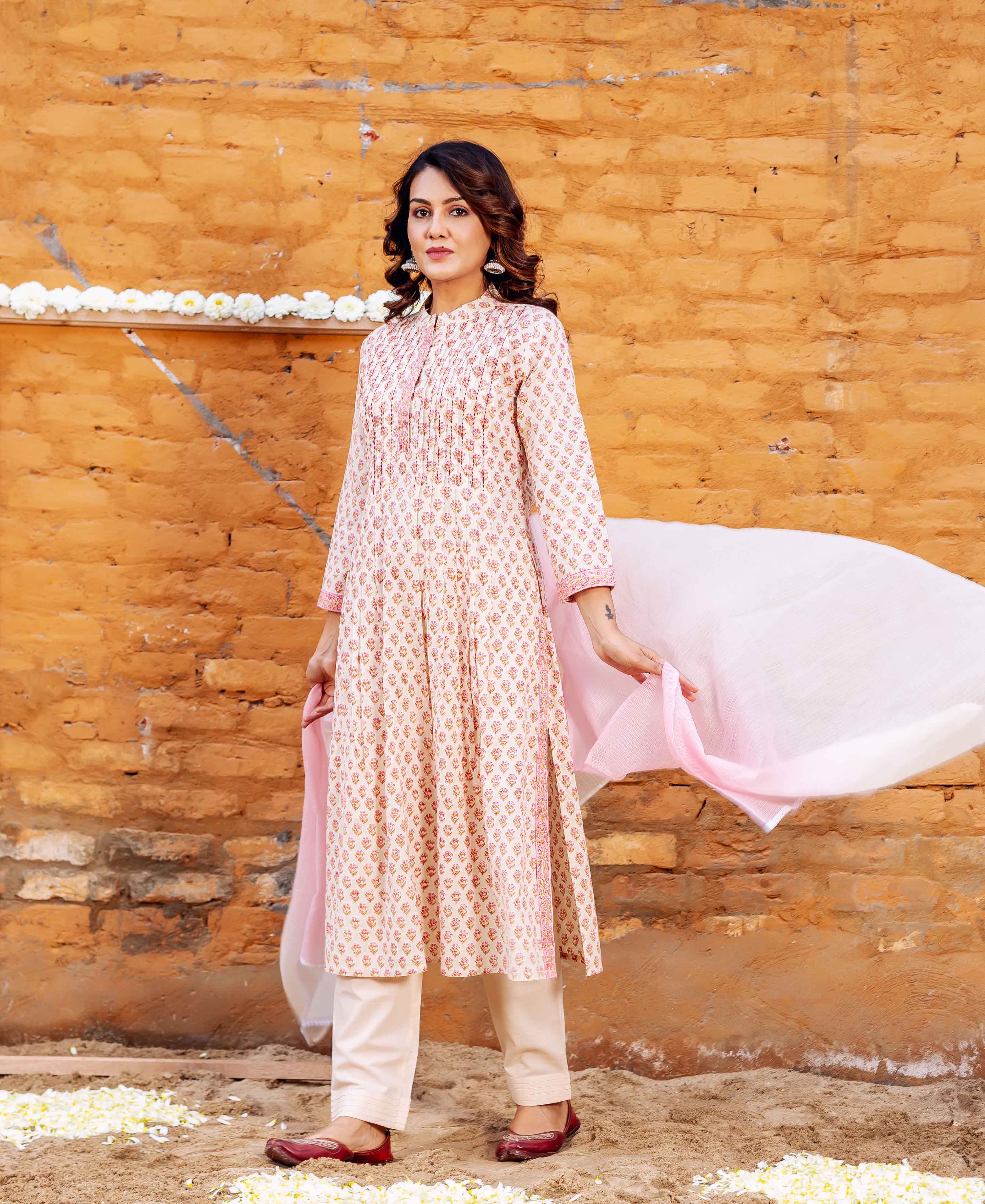 Model poses wearing a cream block-printed kurta, pink floral pattern, with coordinating trousers and dupatta.