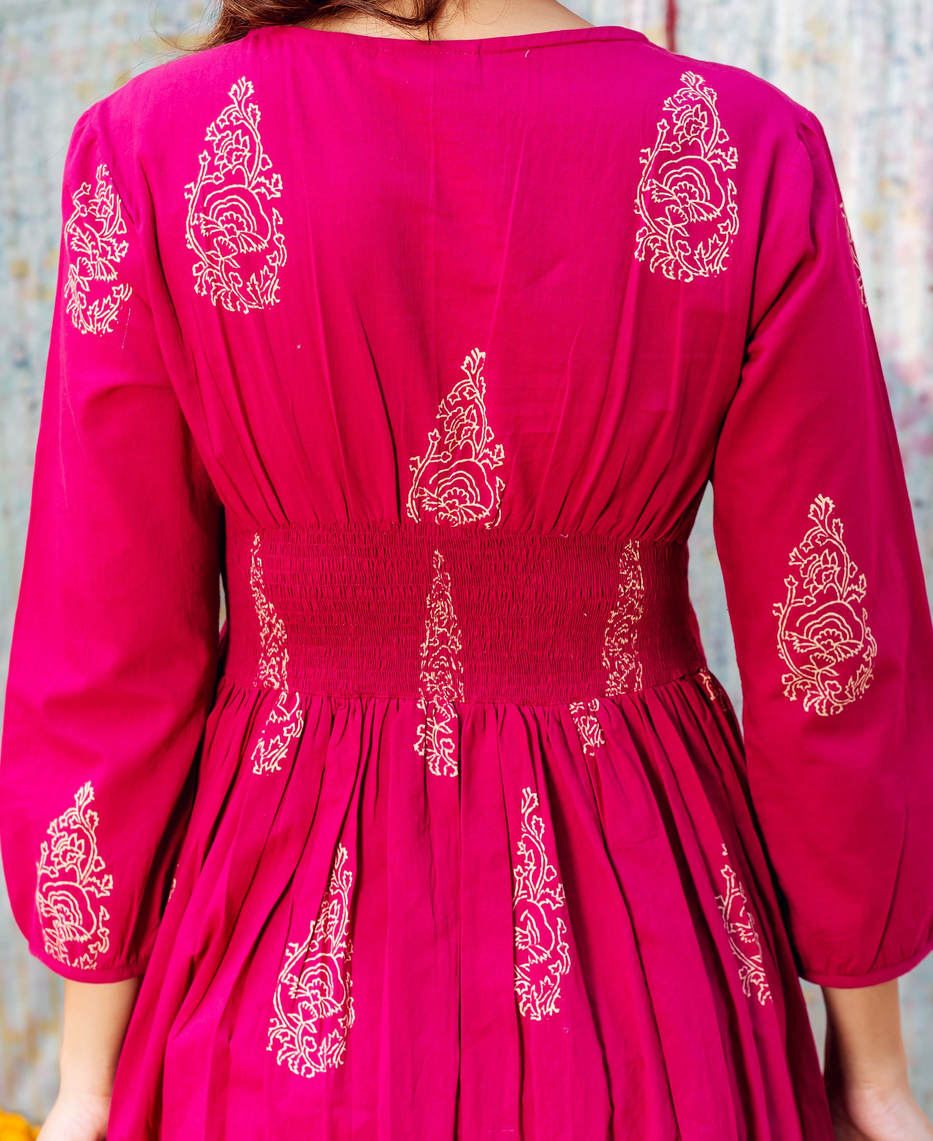 Back of model in a fuchsia hand-block printed dress with cream floral motifs and smocked waist.