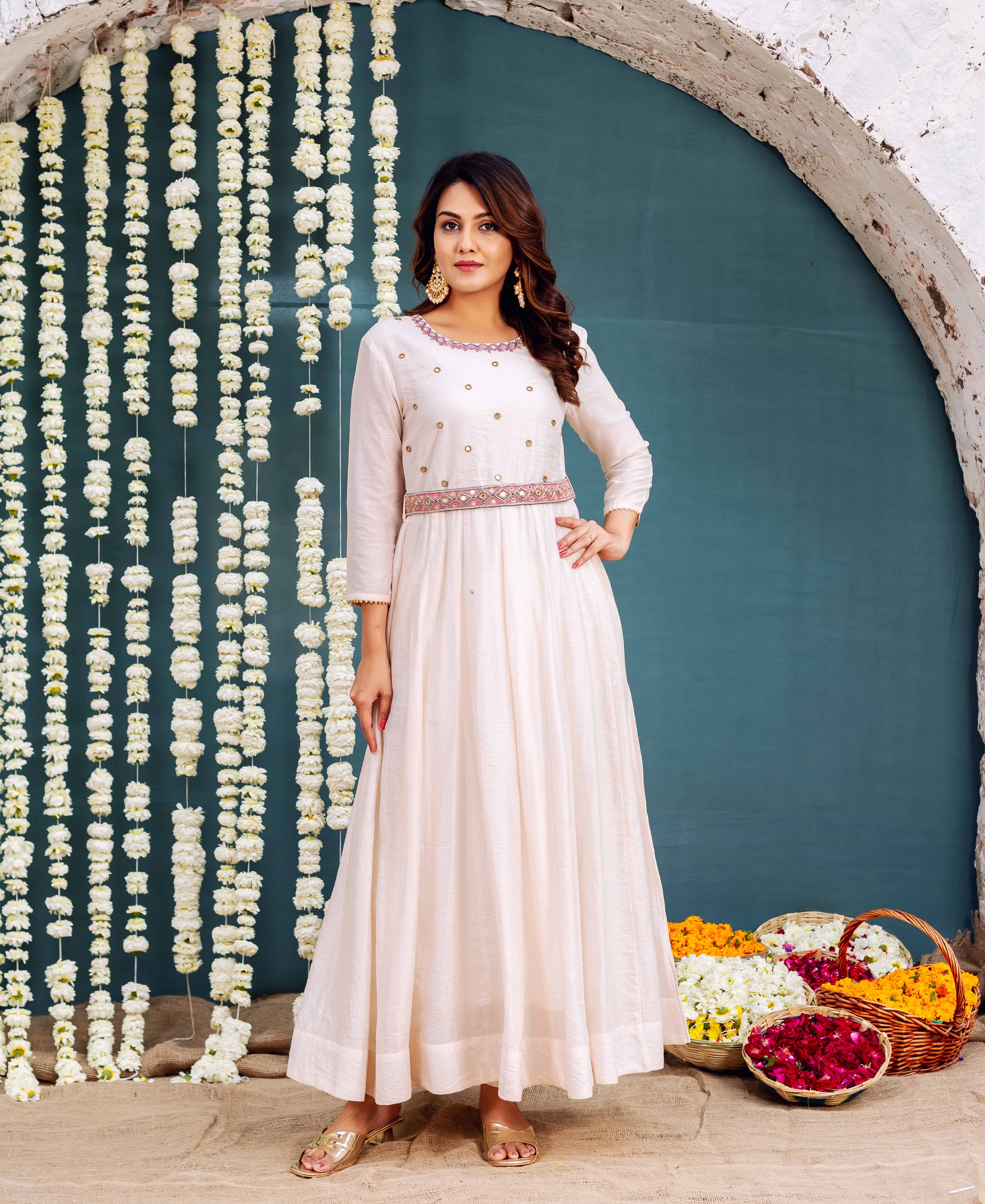 Model wears a pale pink Anarkali dress with gold embellishments and an embroidered waist belt.