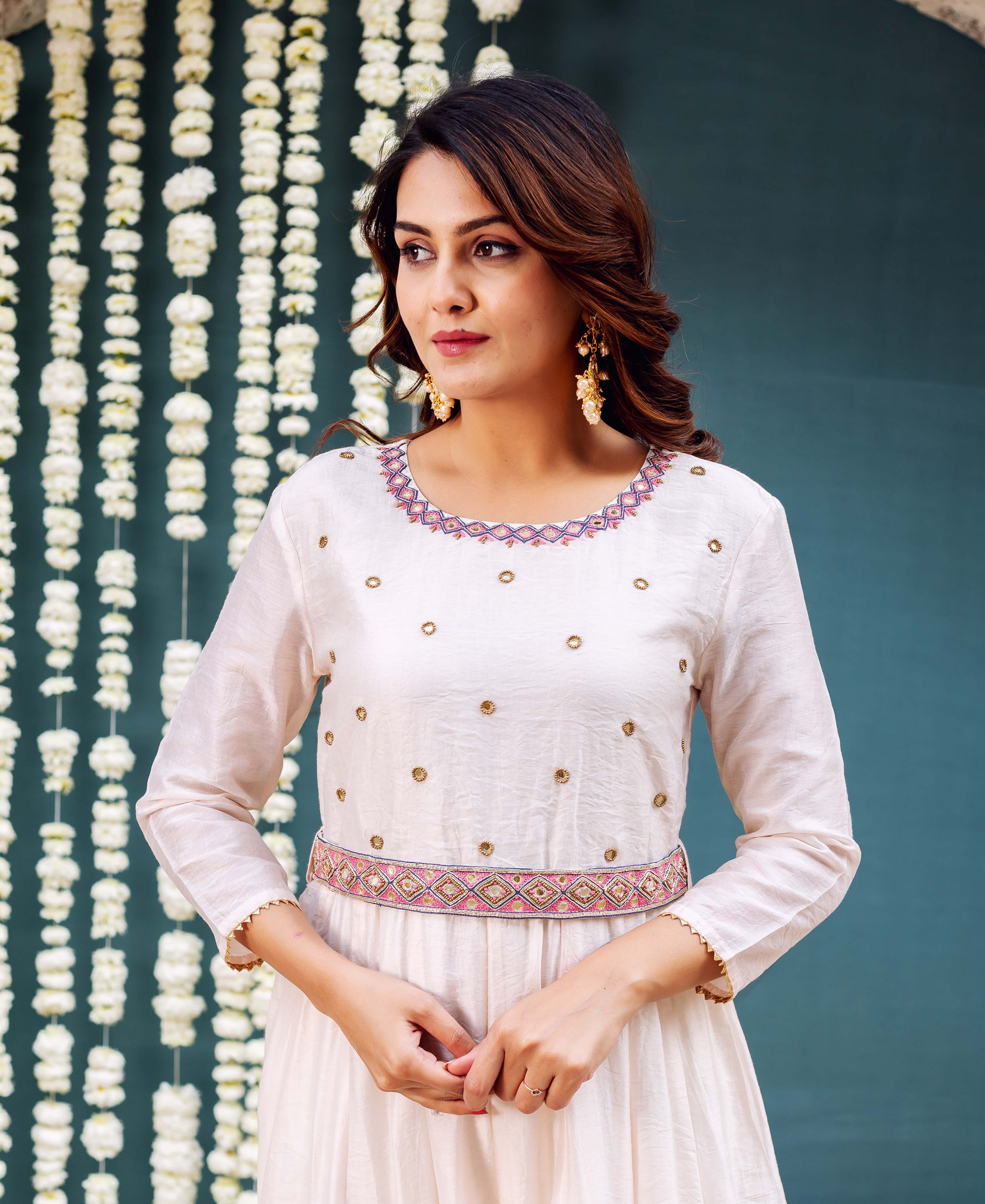Model in an off-white Anarkali dress featuring ethnic geometric patterns and gold embellishments.