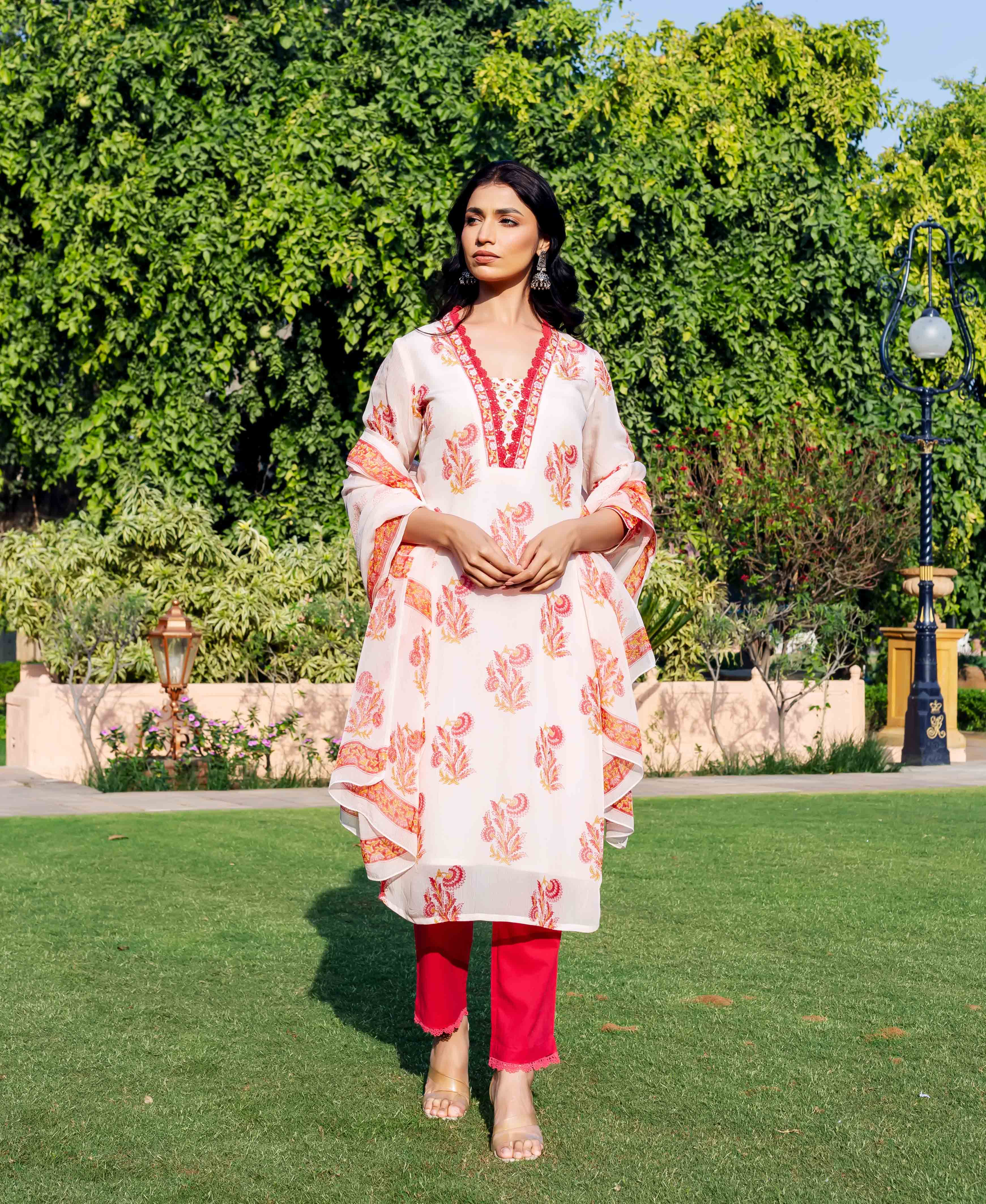 Woman wearing off-white hand-block-printed kurta with orange and pink designs, red trim and pants.