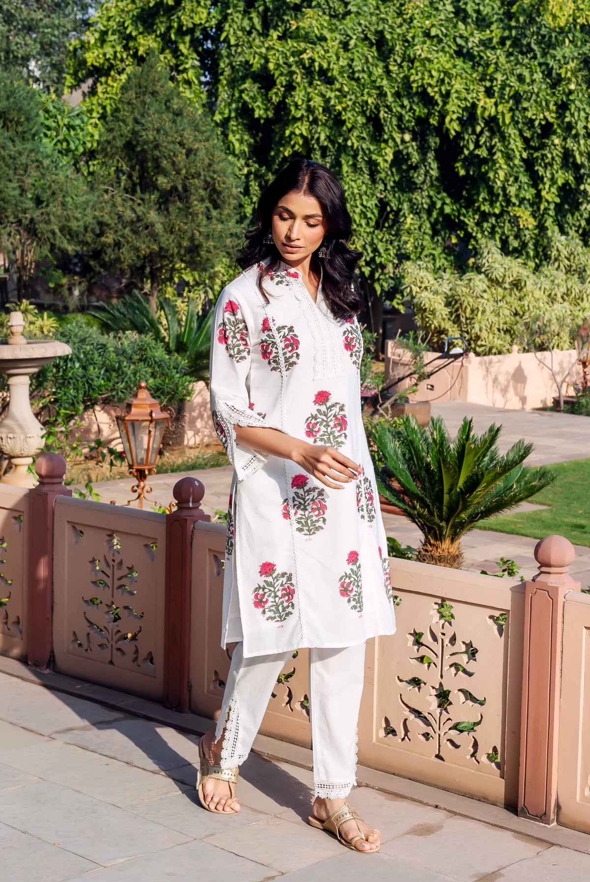 Woman in white hand-block-printed kurta and pants with pink floral patterns and green details.