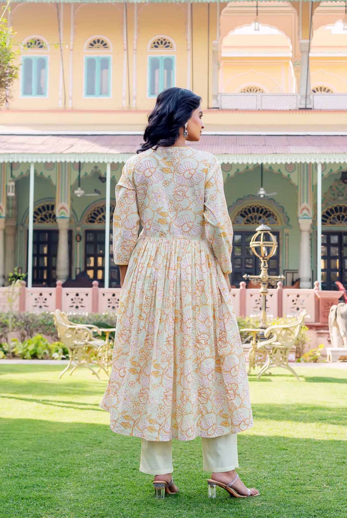 Rear view of model in pale green hand-block printed floral cotton kurta and cream pants.