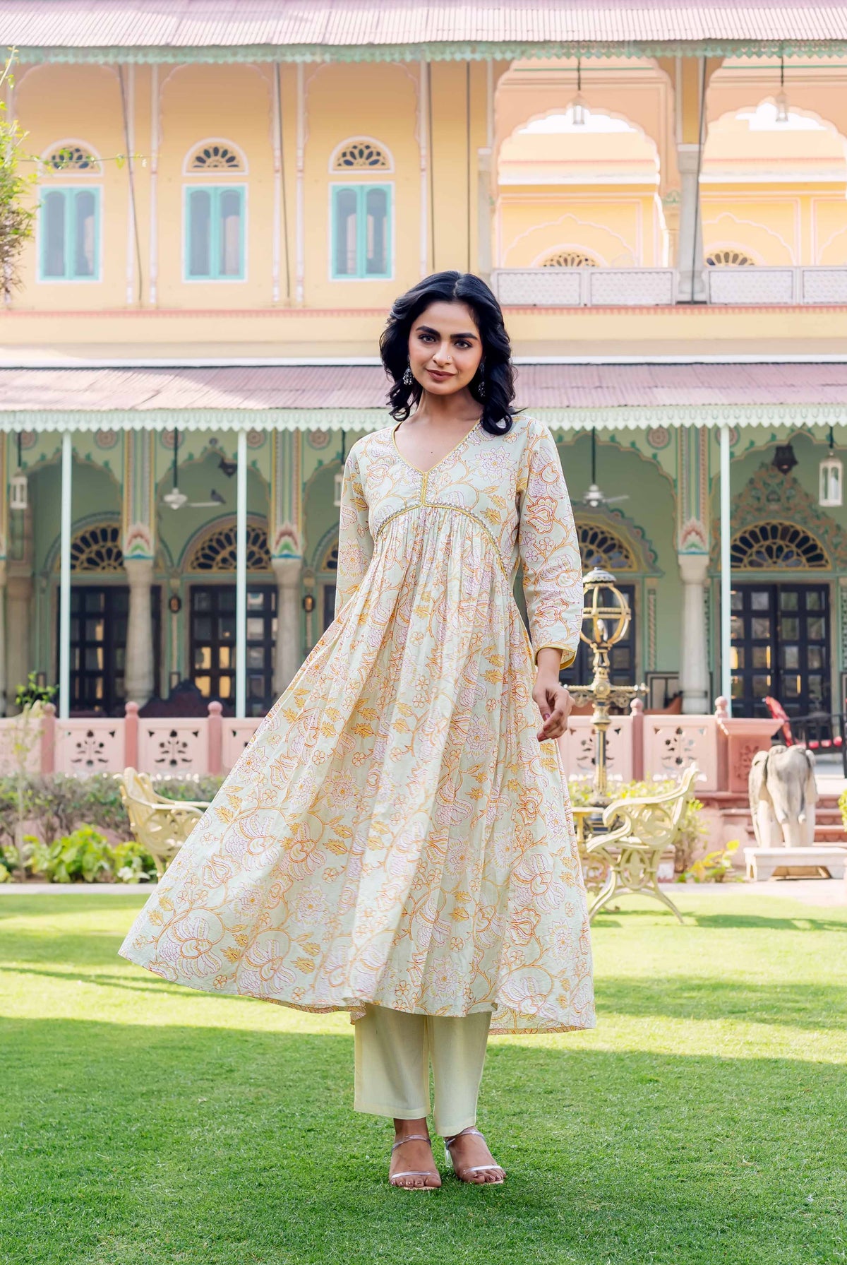 Model in flowy light green kurta with orange and pink floral print, pale pants.
