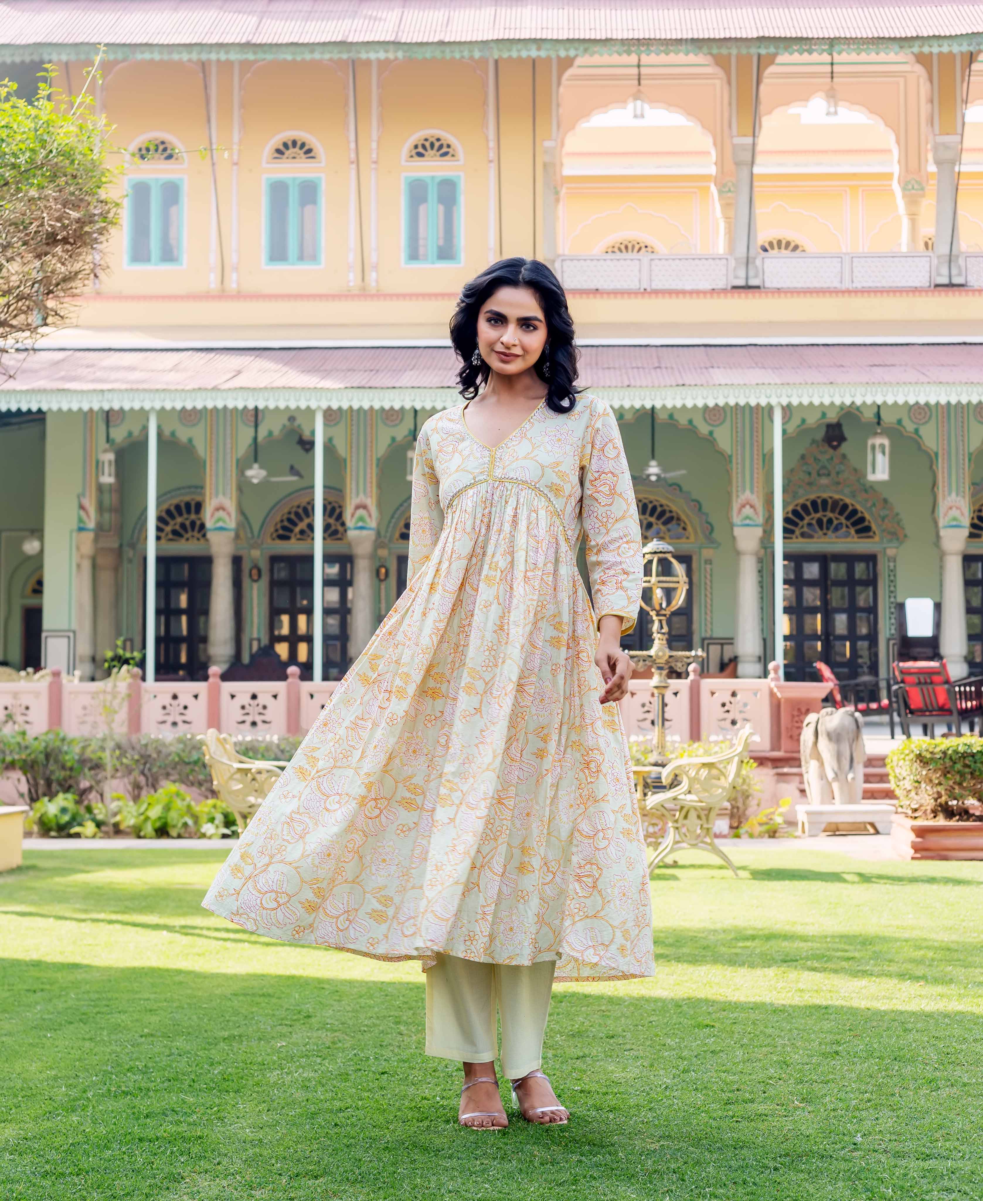 Model in flowy light green kurta with orange and pink floral print, pale pants.