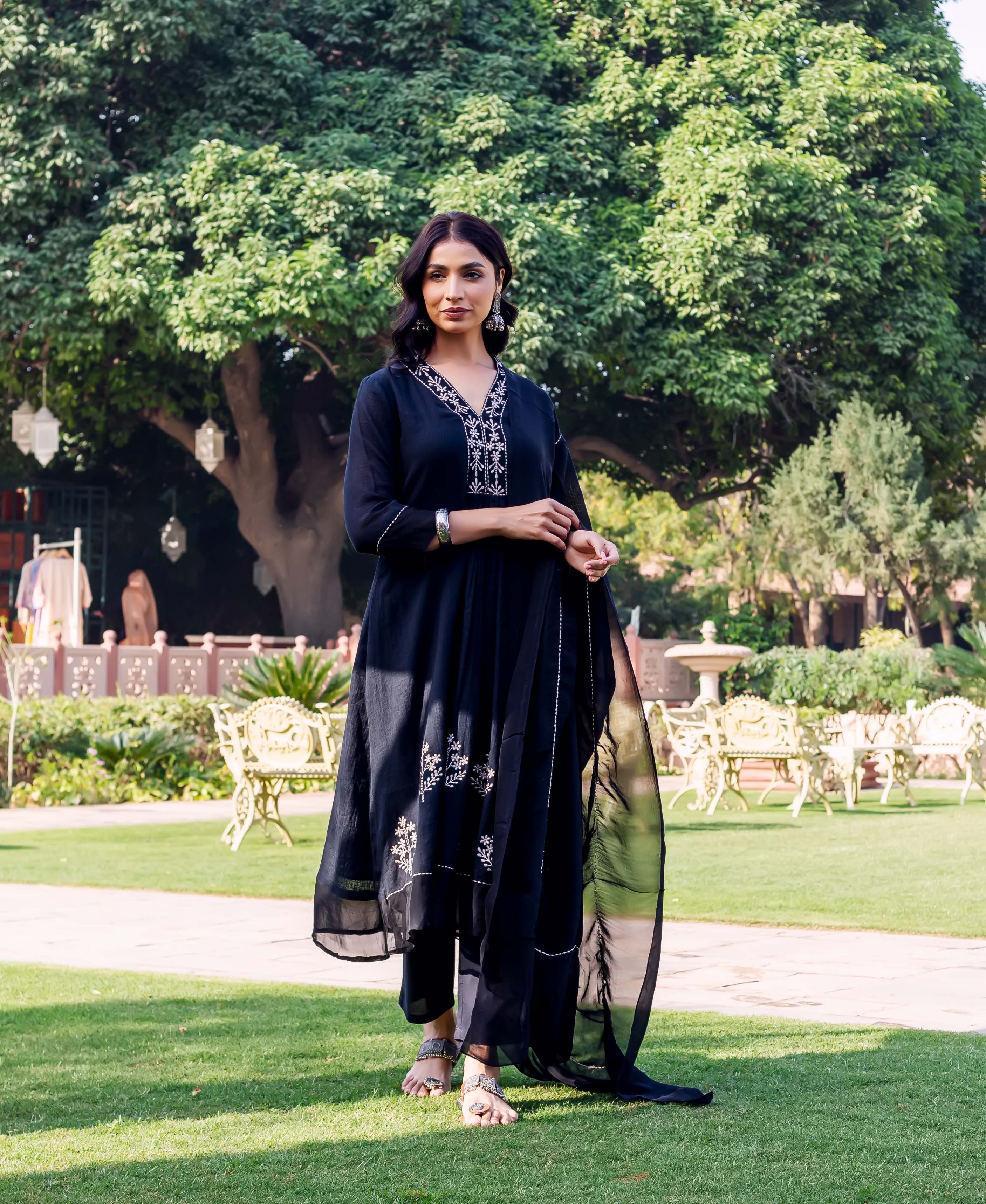 Woman models a black ethnic kurta set with white embroidered V-neck and lower patterns.