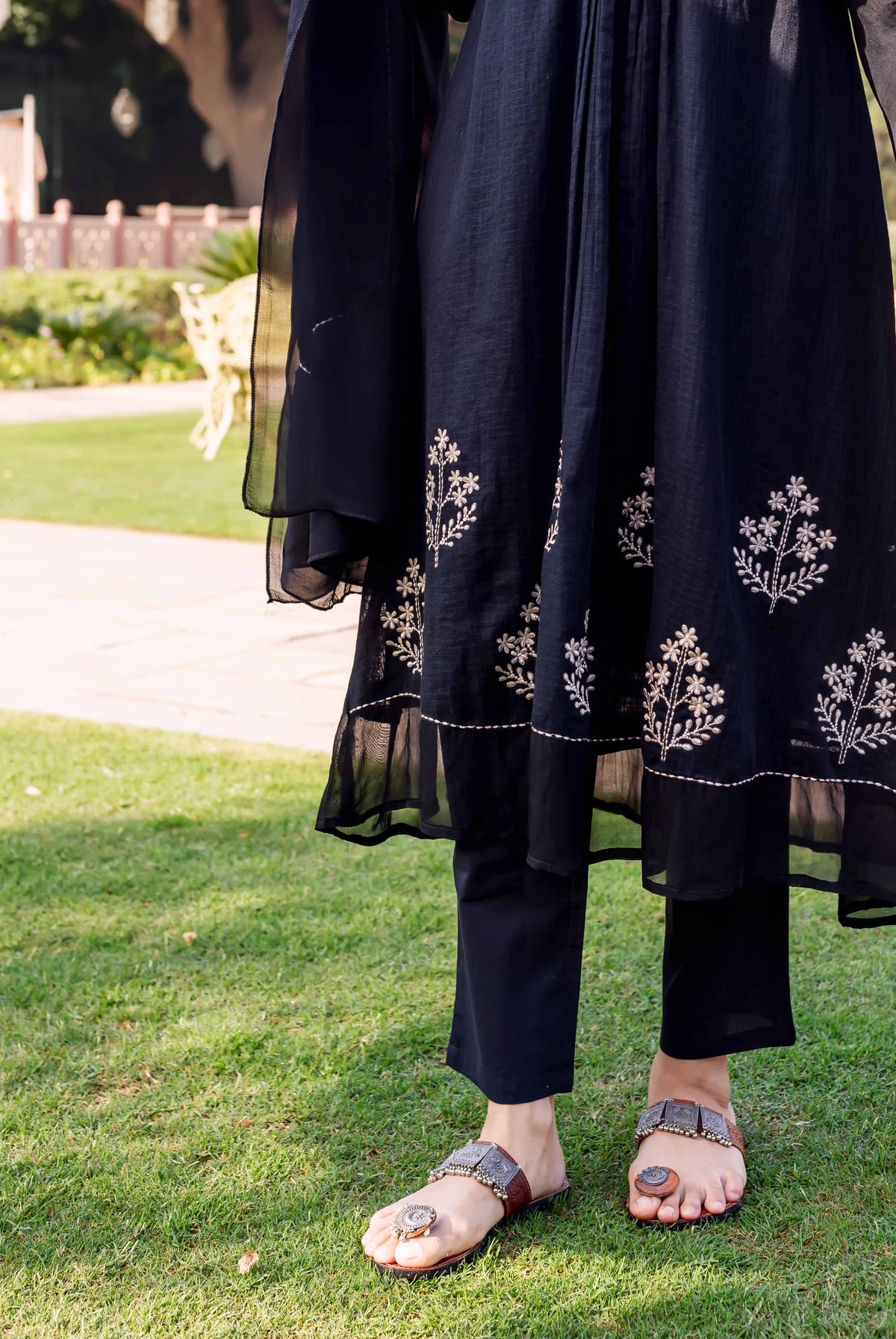 Lower shot of model wearing black kurta with white floral embroidery and black pants.