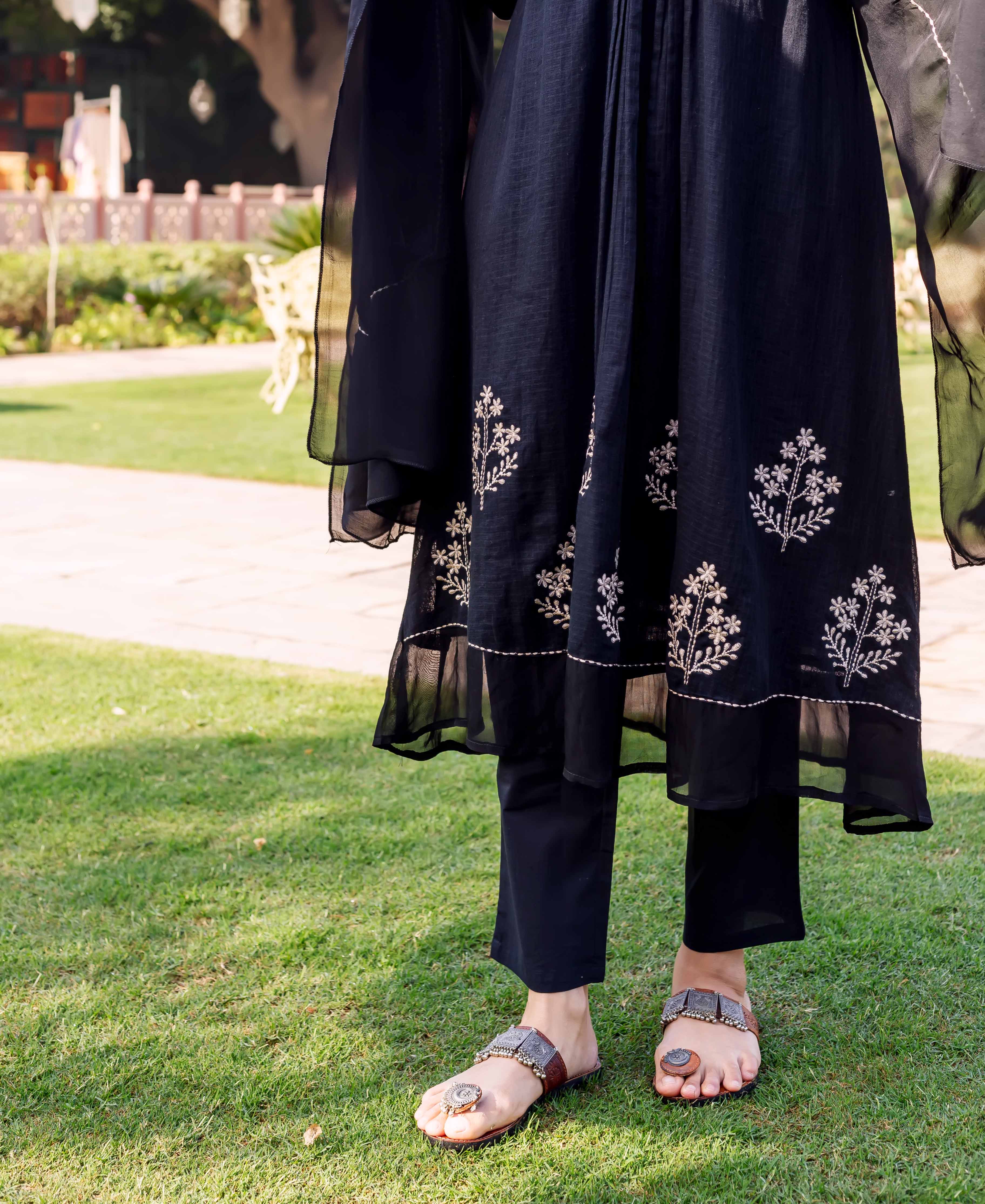 Lower shot of model wearing black kurta with white floral embroidery and black pants.