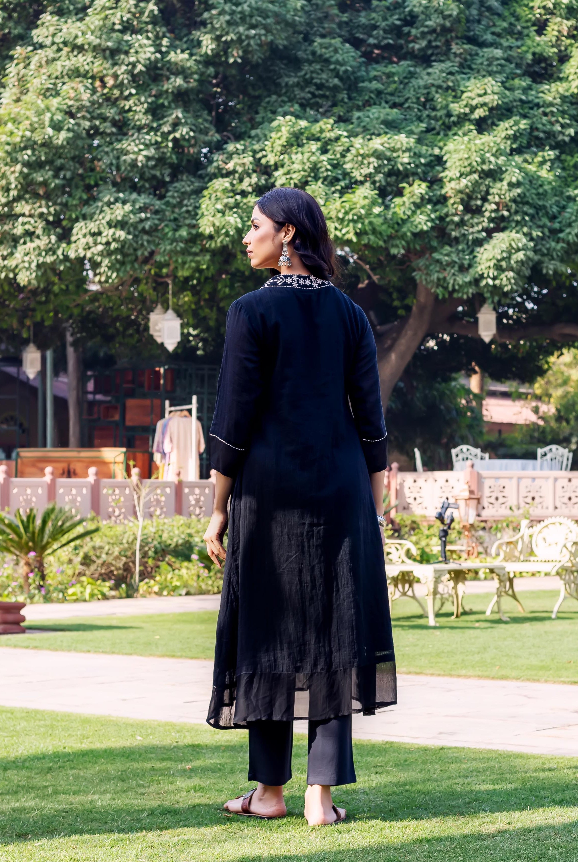 Back view of model wearing black kurta with white embroidered neckline and black pants.
