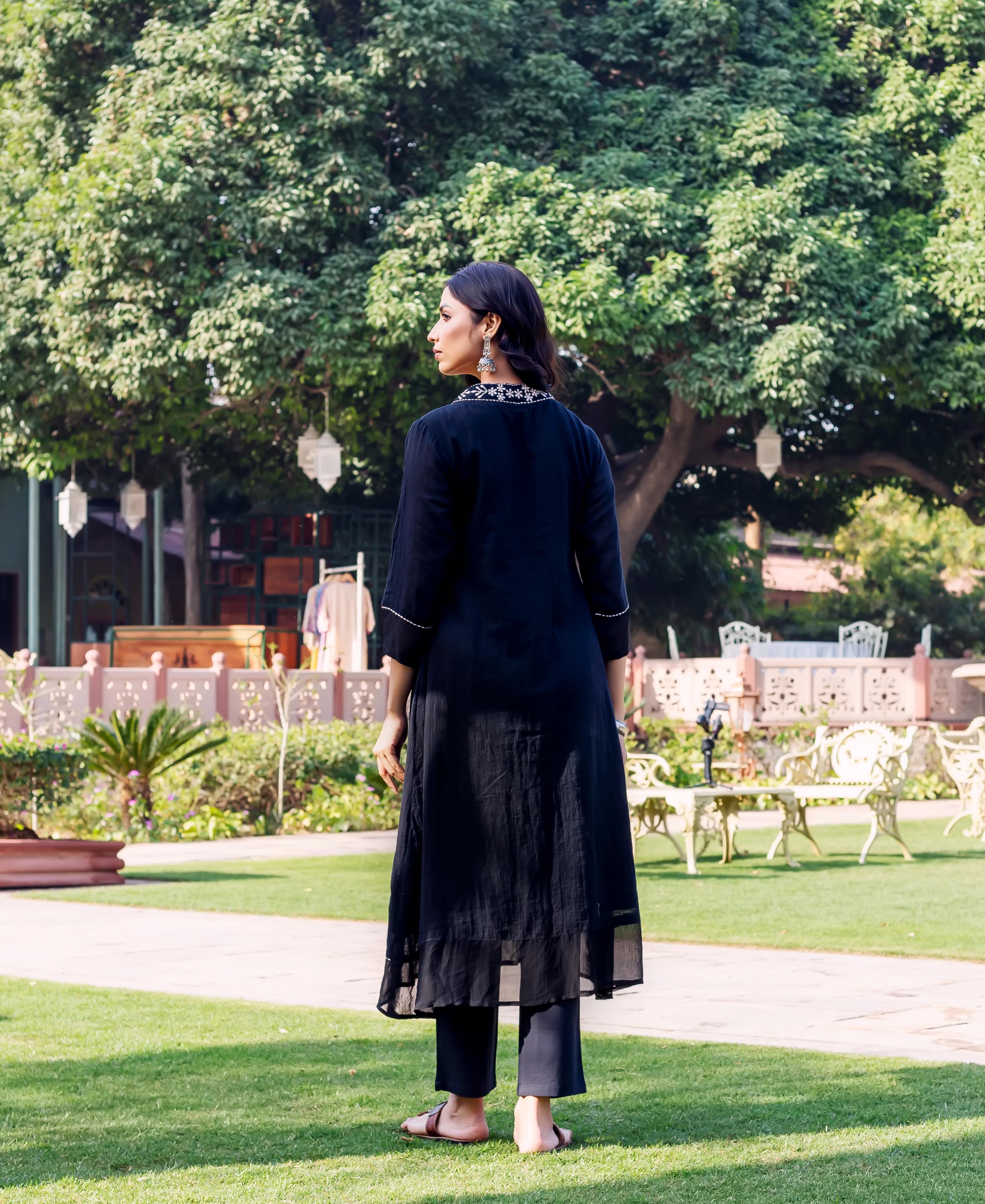 Back view of model wearing black kurta with white embroidered neckline and black pants.