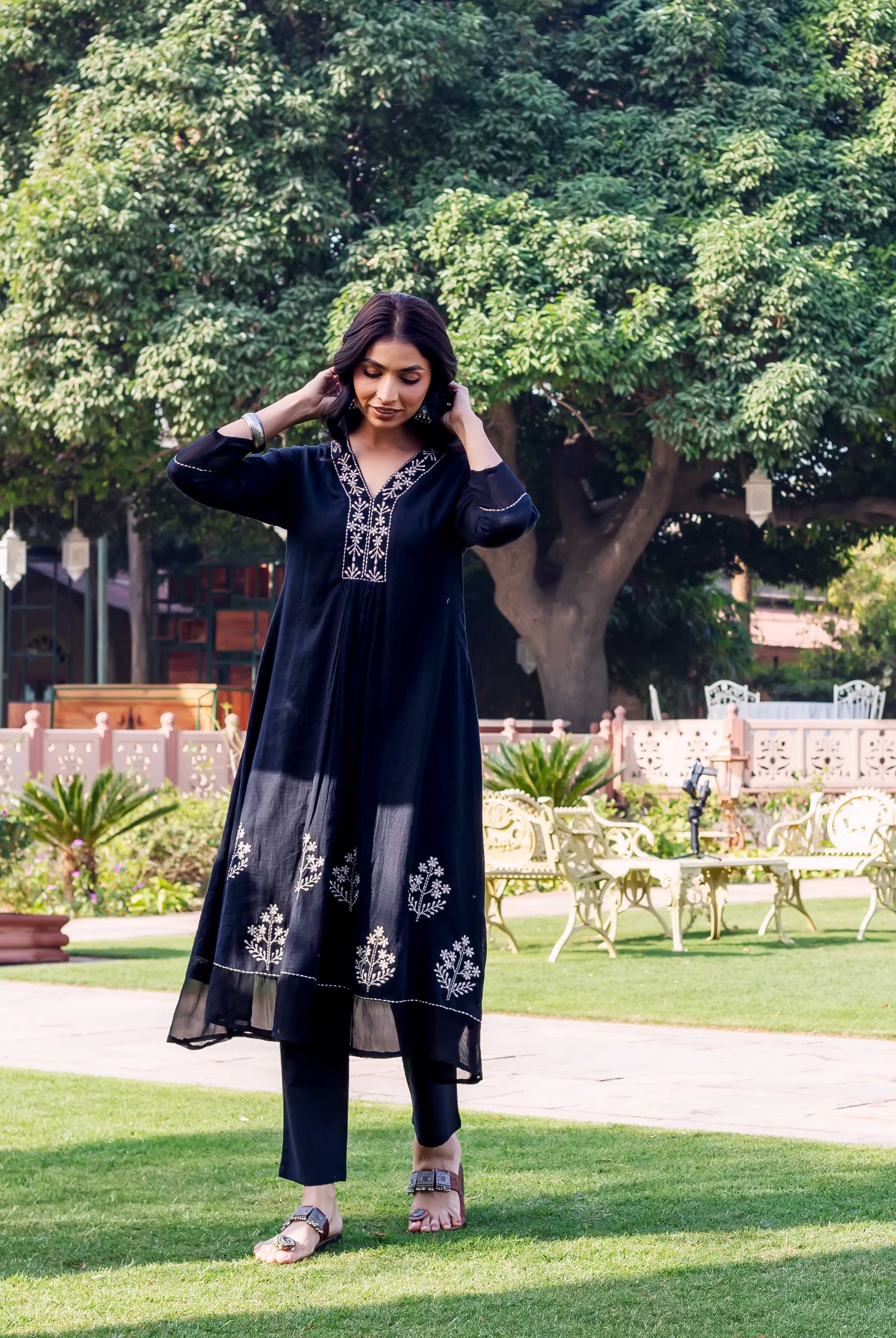Woman standing in black embroidered kurta set, featuring white floral patterns on neckline and hem.