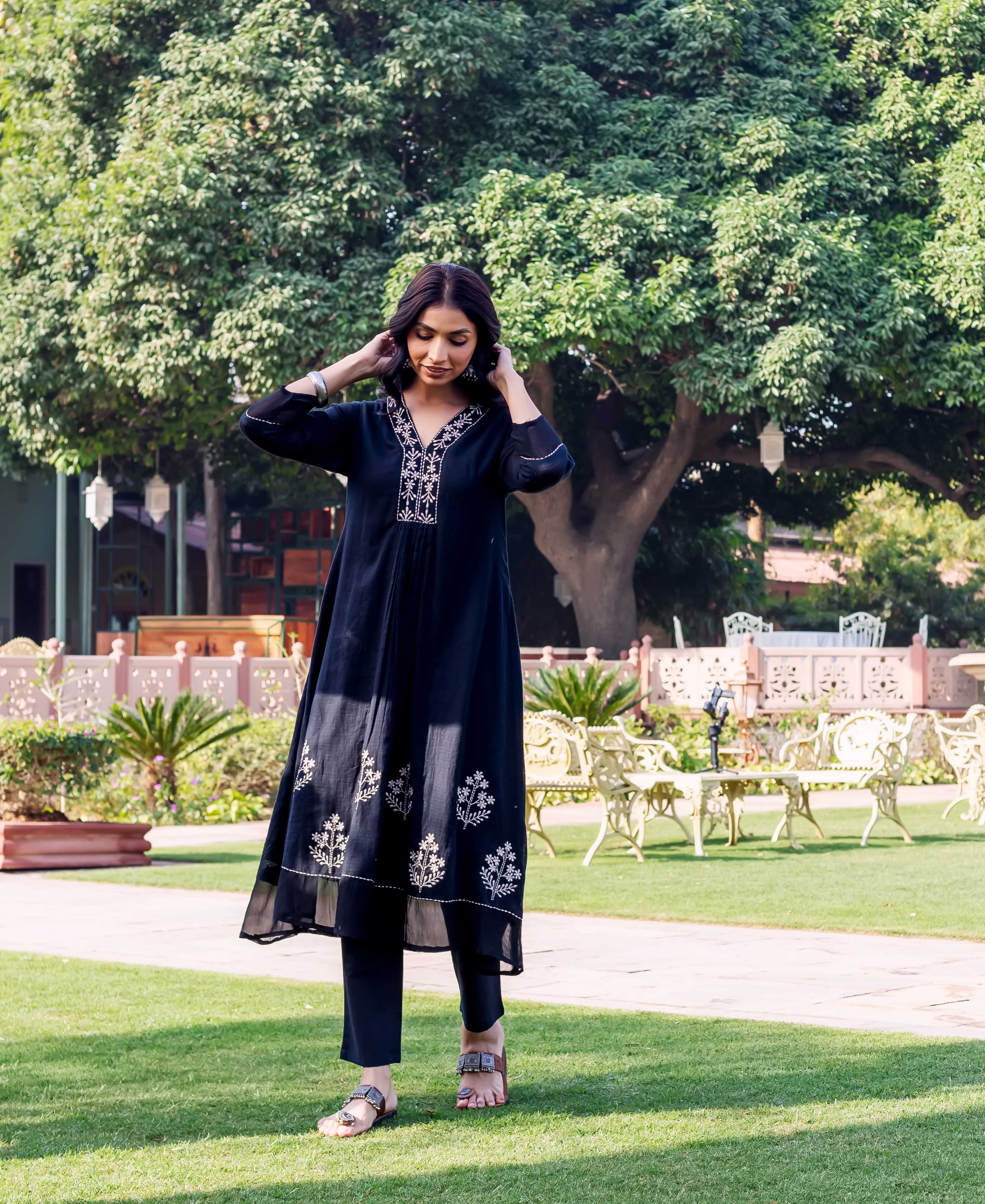 Woman standing in black embroidered kurta set, featuring white floral patterns on neckline and hem.