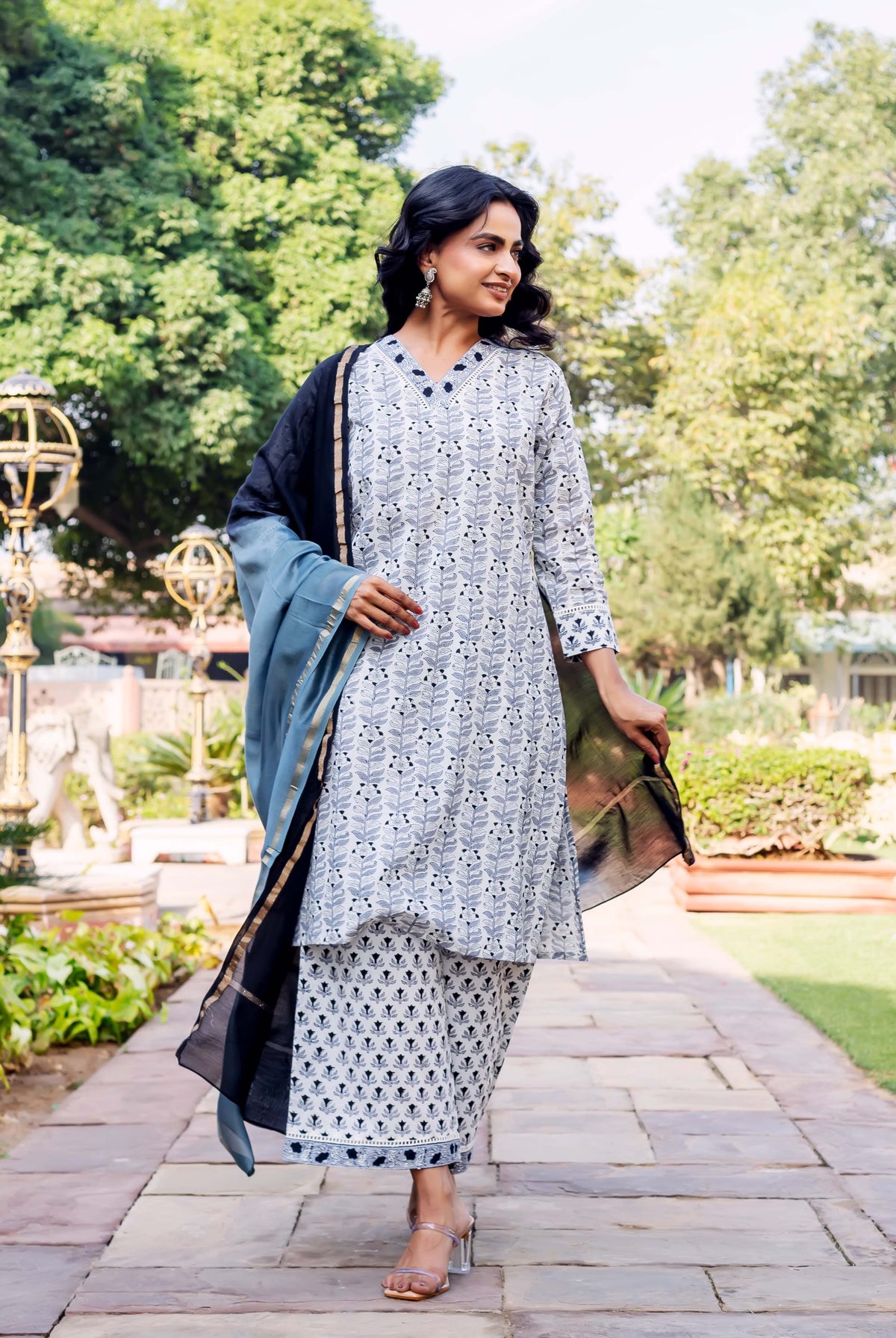 Model in grey block-printed kurta, geometric palazzo pants, and black-blue dupatta, walking outdoors.