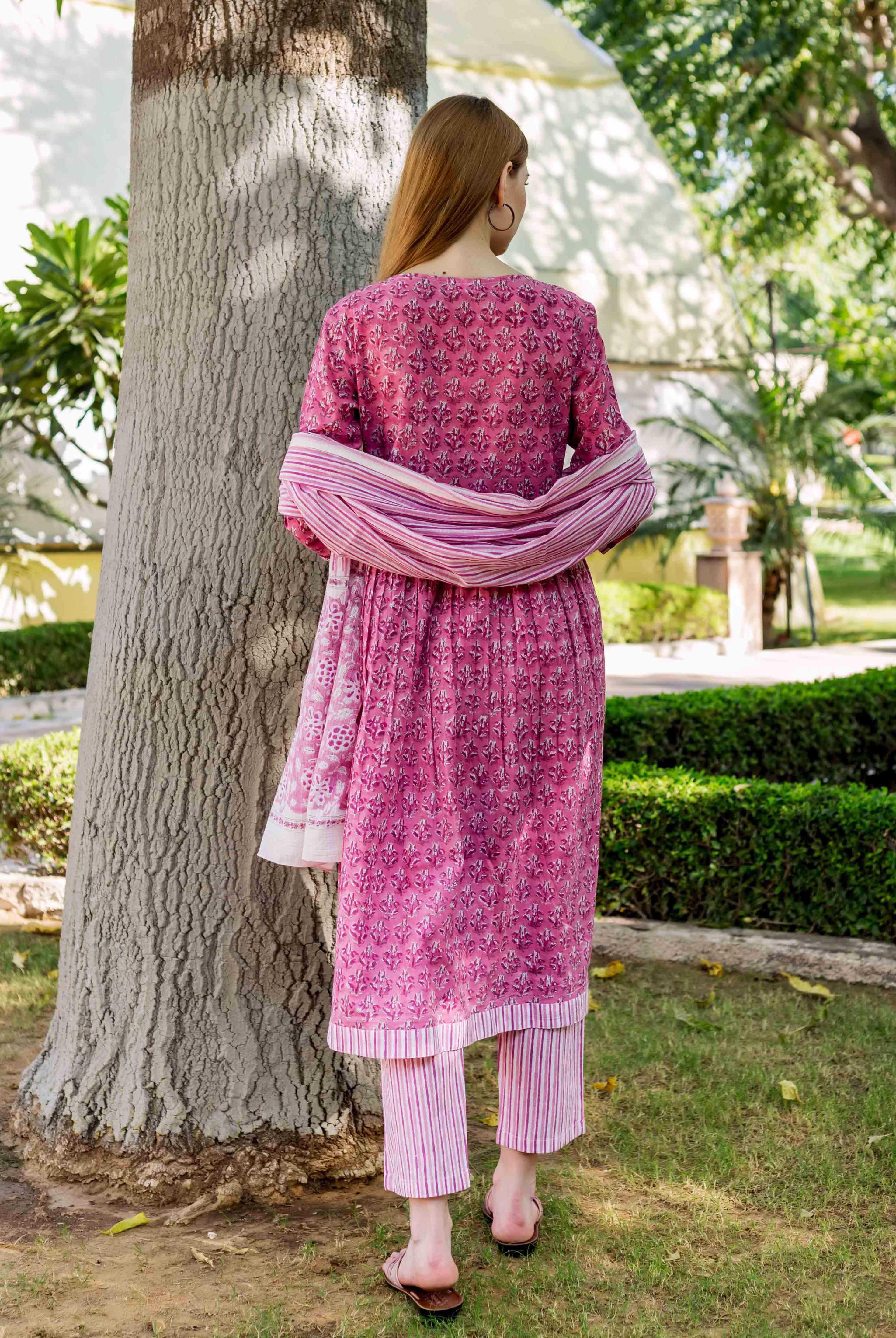 Back view of model wearing pink floral block print A-line kurta with striped pants and dupatta.