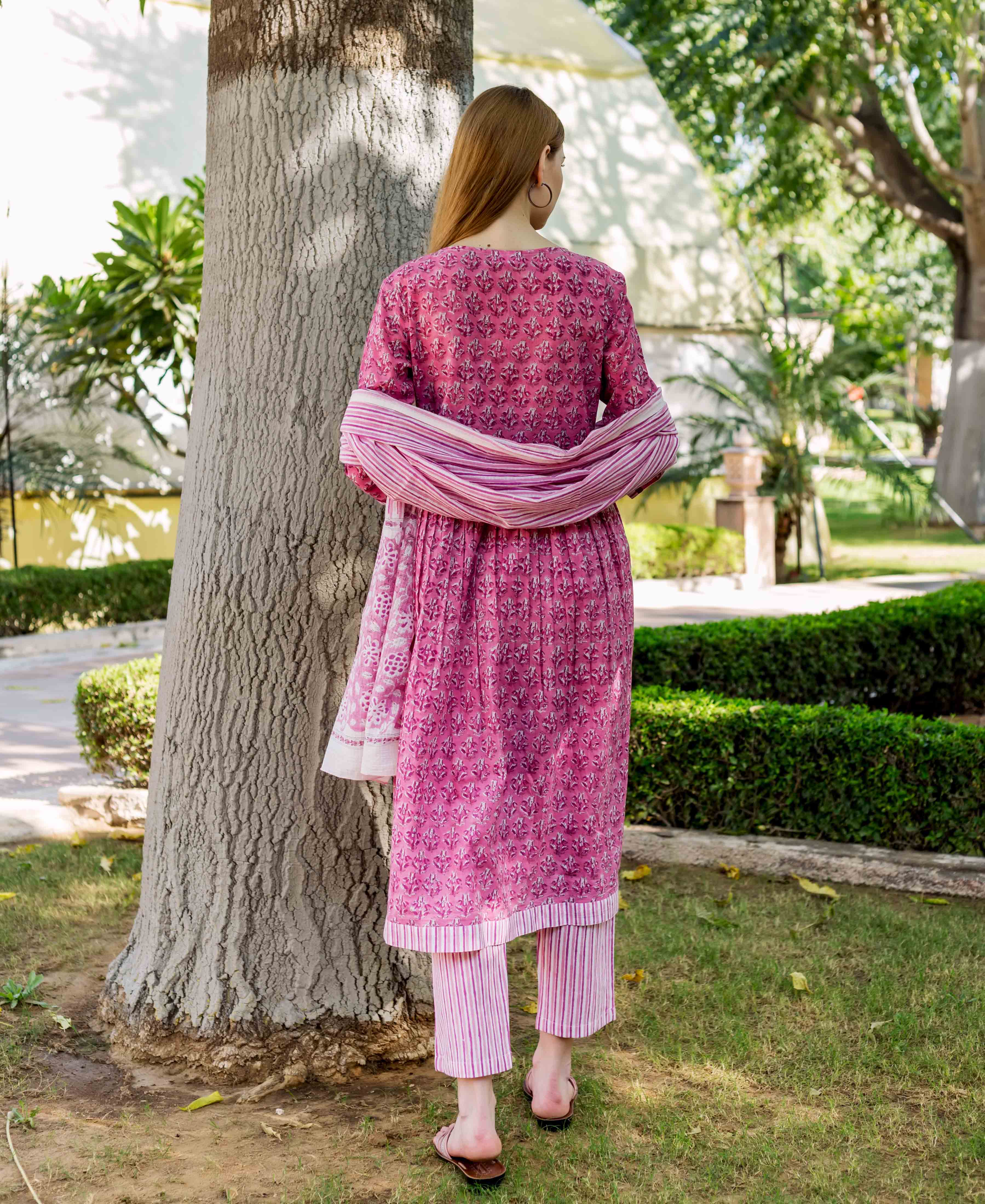 Back view of model wearing pink floral block print A-line kurta with striped pants and dupatta.