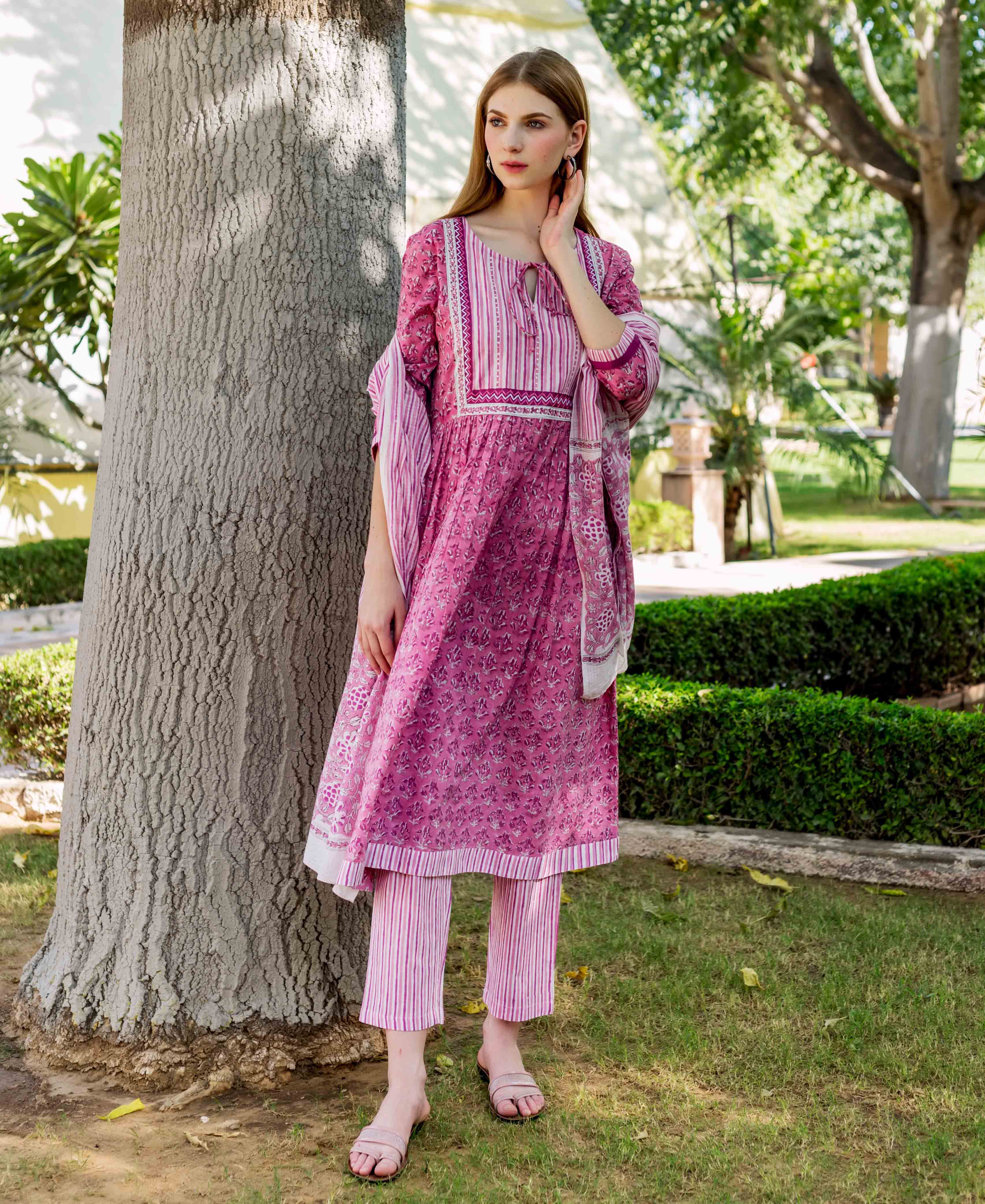Front view model in pink floral hand-block-printed A-line kurta with striped pants and dupatta.