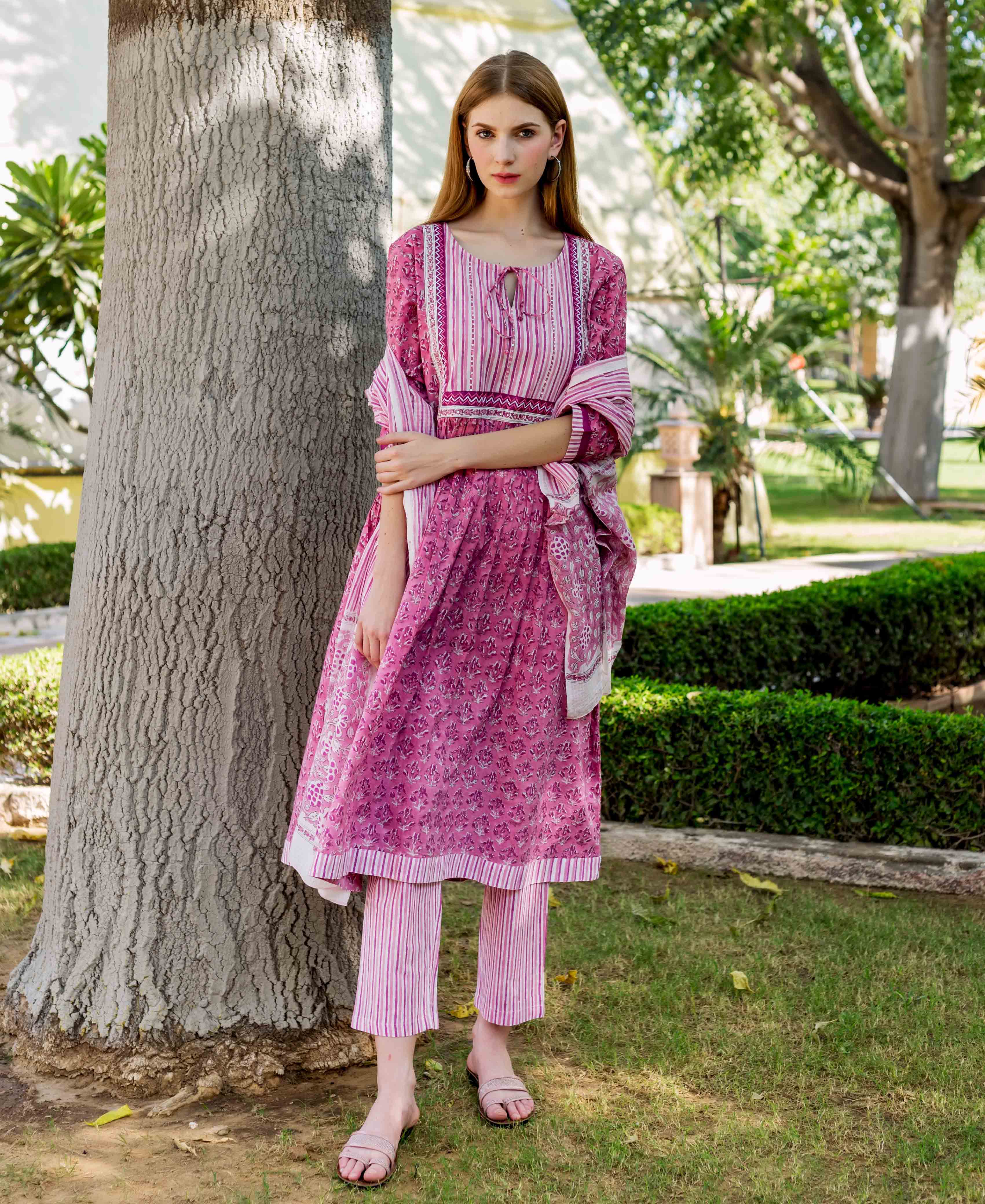 Model standing, wearing a pink hand-block printed A-line kurta, striped pants and matching dupatta.