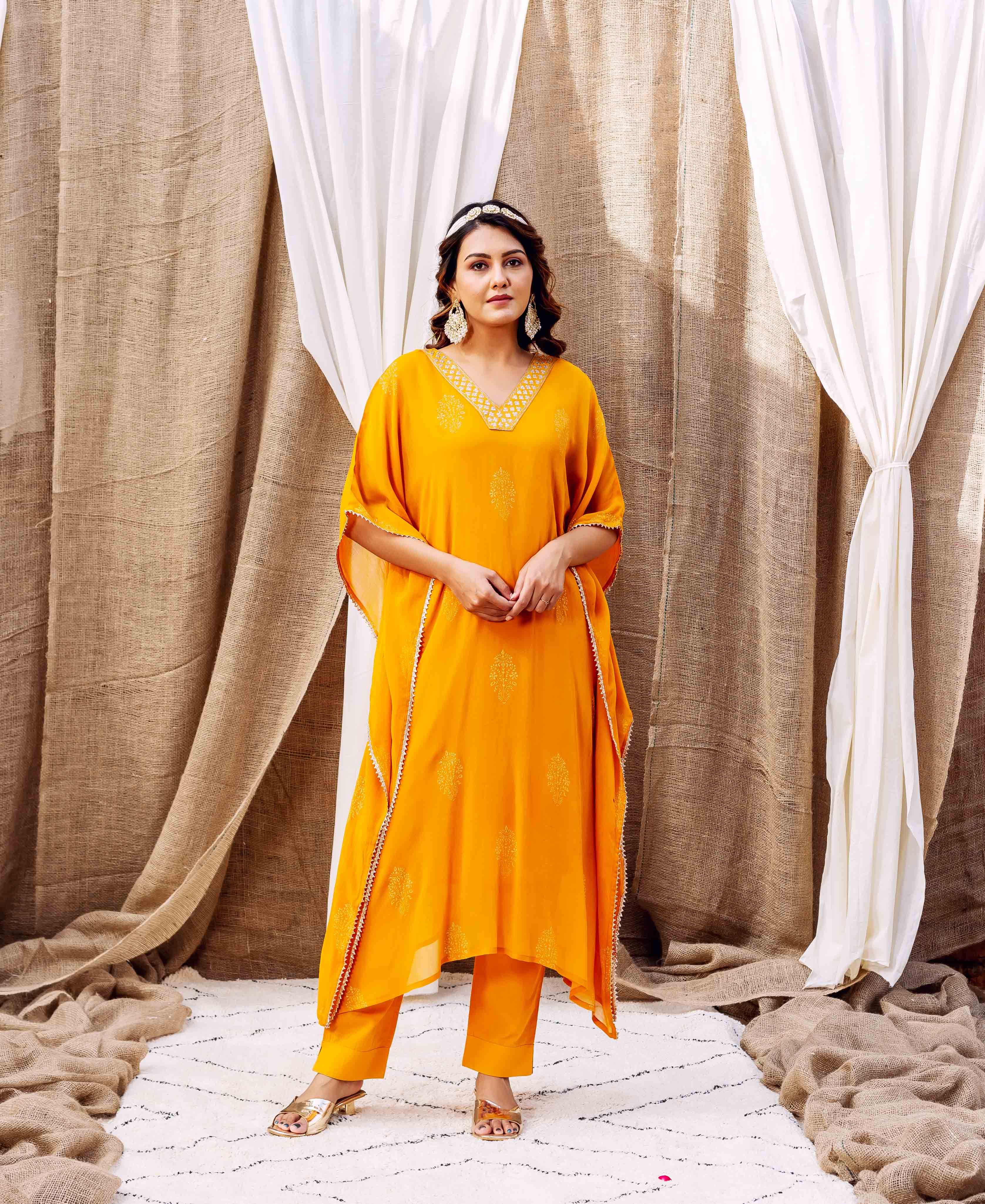 Full-length shot of model wearing a bright yellow embroidered kaftan set with matching trousers.