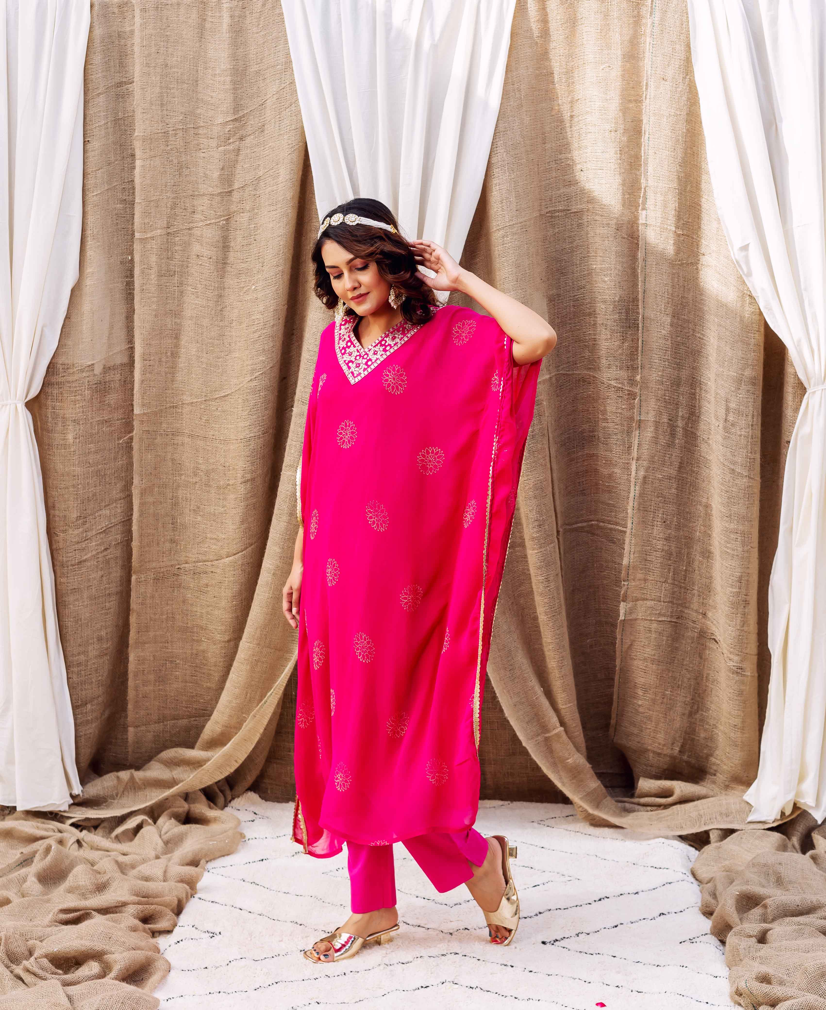 Model wears a magenta embroidered kaftan with gold floral prints and matching pants.