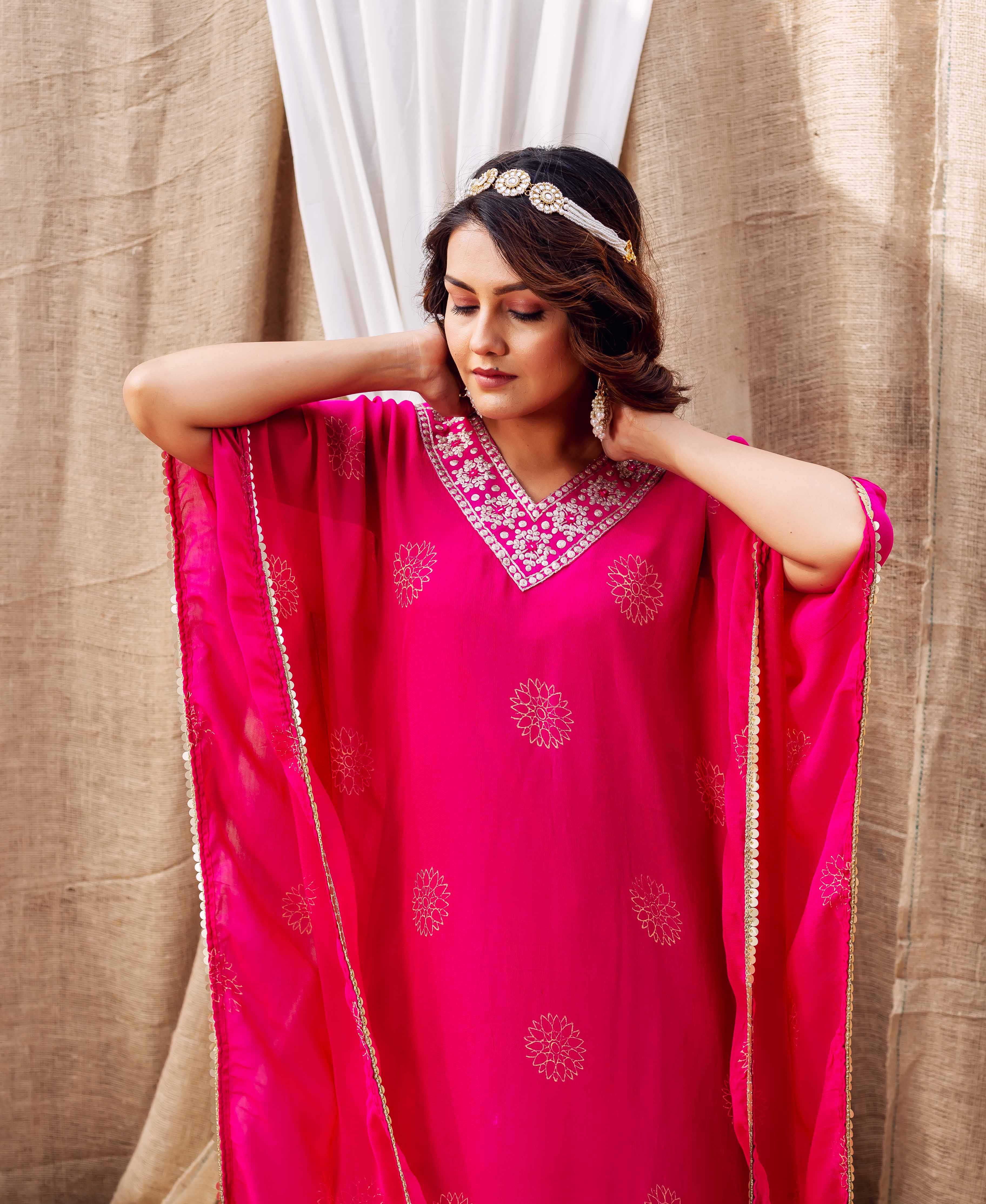 Magenta kaftan on model, with elaborate white embroidered neckline and golden floral motifs.
