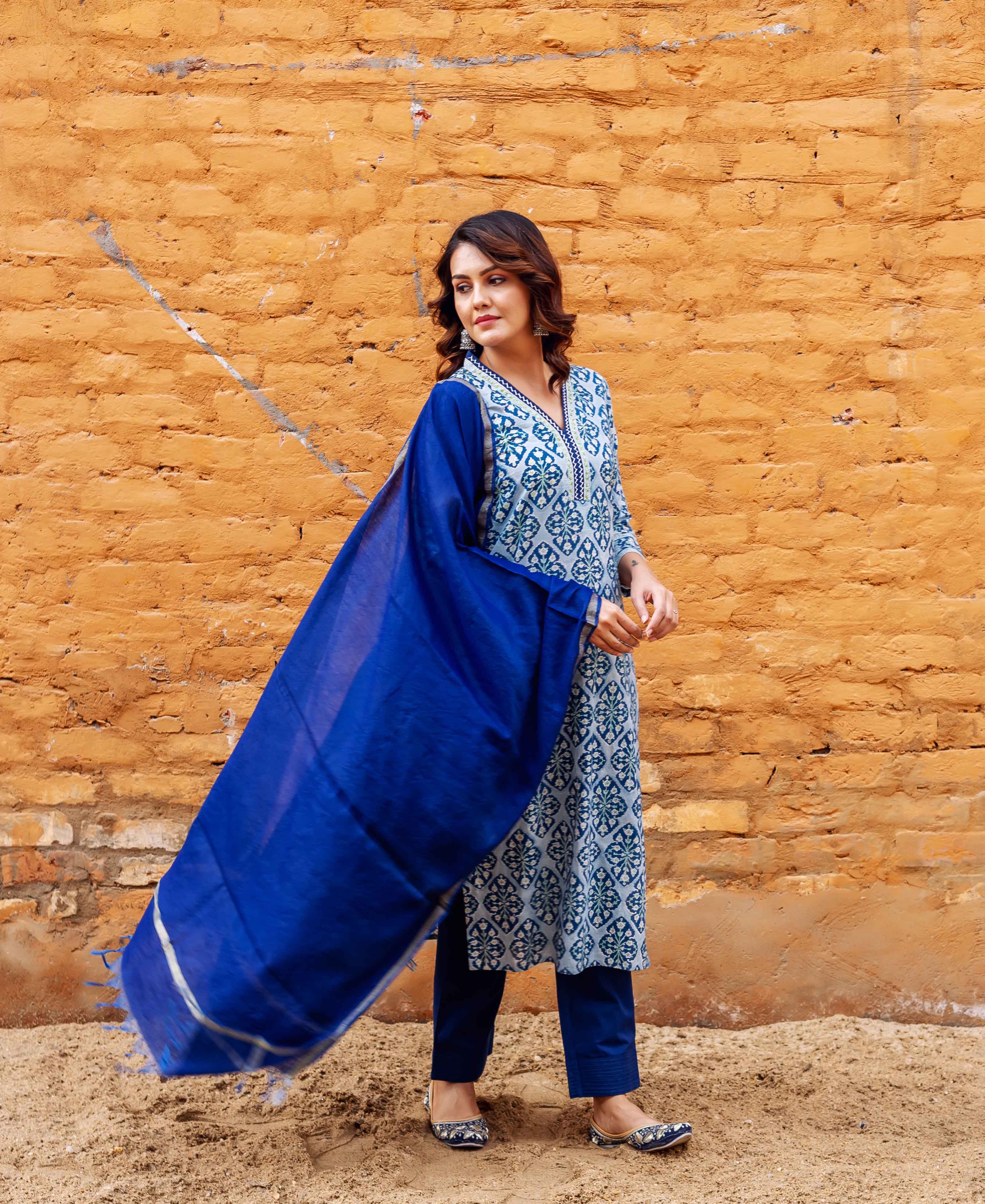Model stands wearing a block-printed blue kurta set with a vibrant plain indigo dupatta flowing.