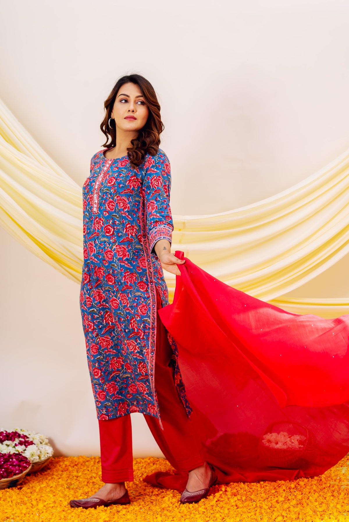Full shot of woman in blue floral print kurta, red bottoms, and flowy red dupatta.