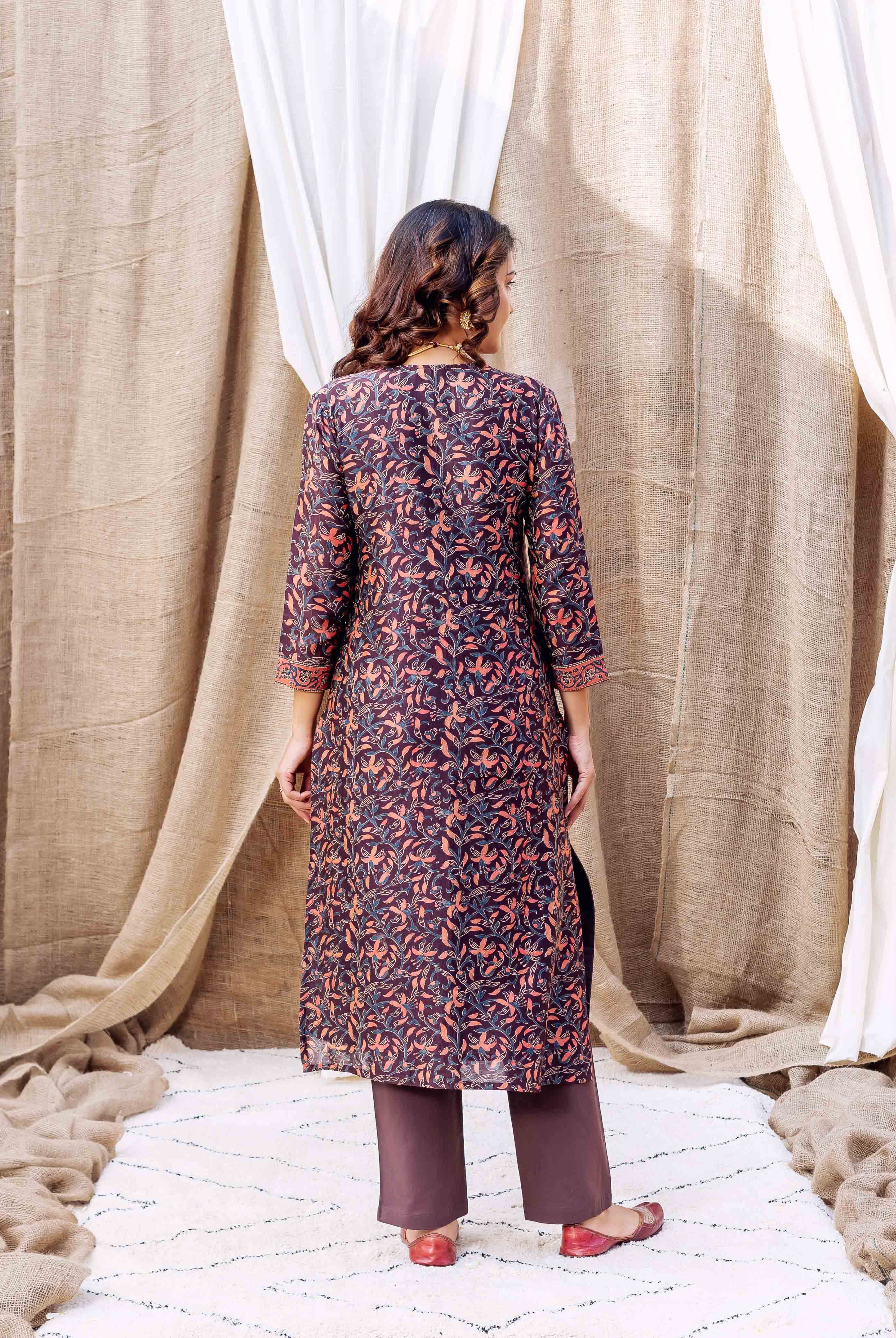 Woman wears long brown silk kurta with orange and blue floral hand-block print and brown pants.