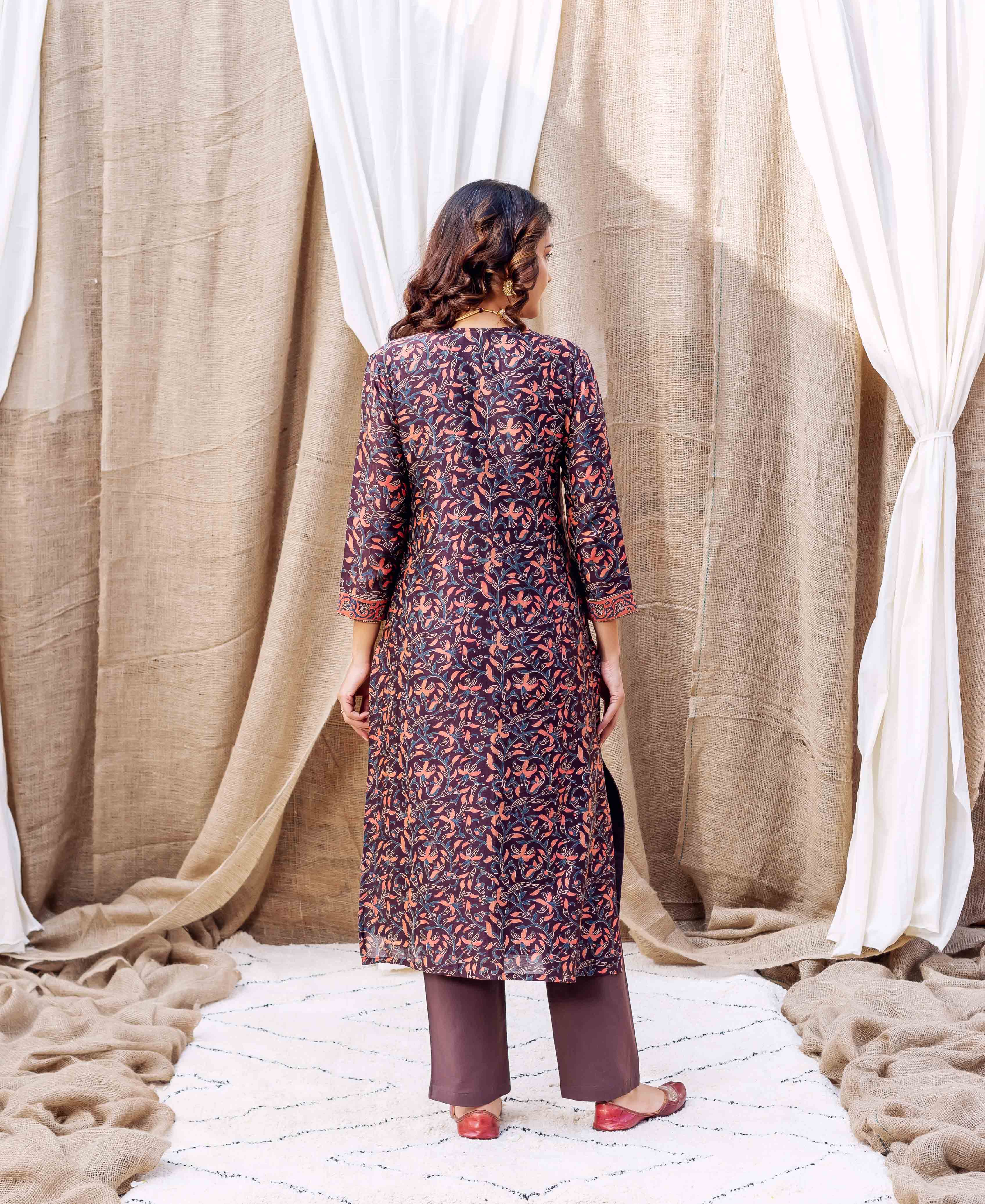 Woman wears long brown silk kurta with orange and blue floral hand-block print and brown pants.