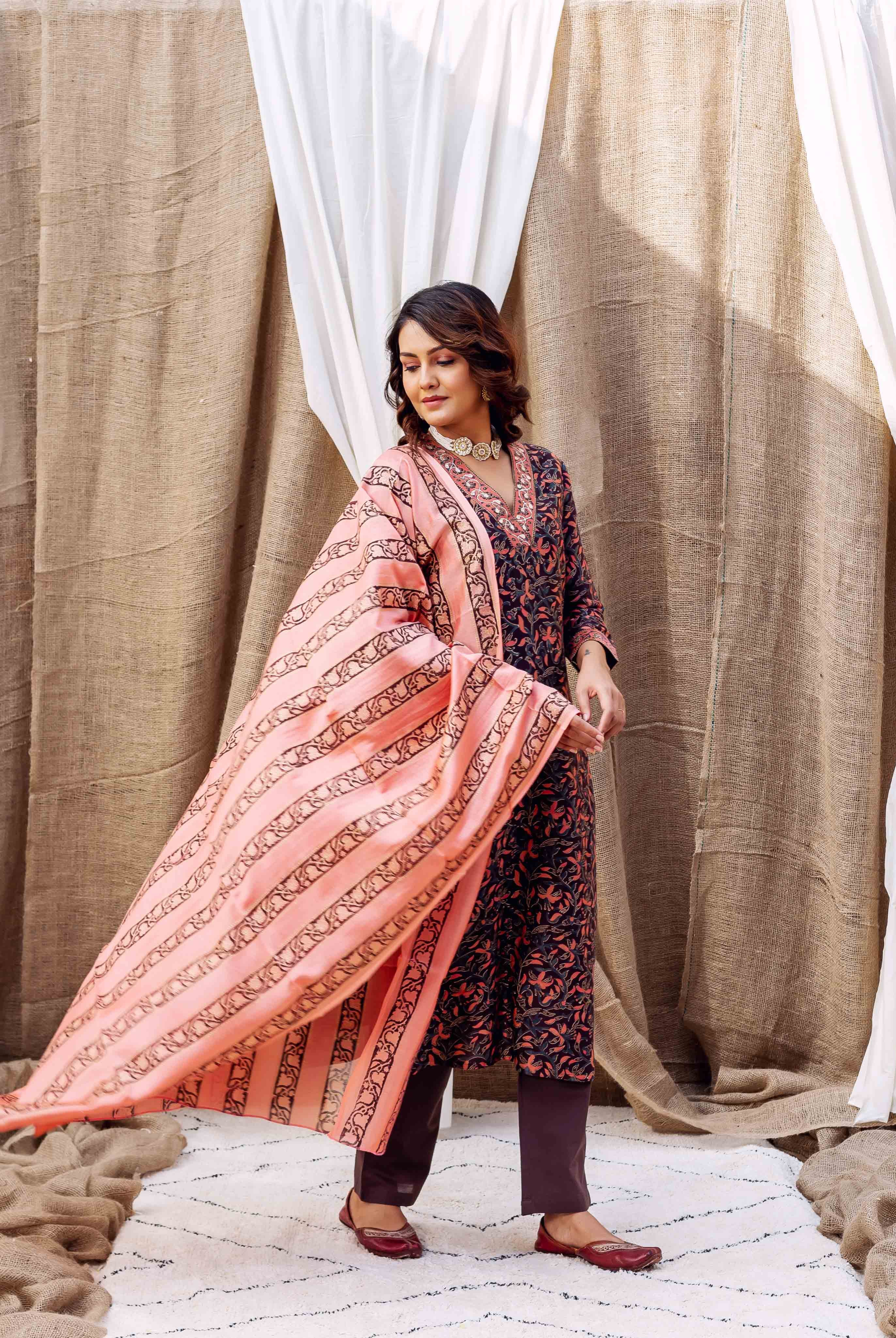 Model in dark floral print kurta set with flowing peach striped and floral dupatta.