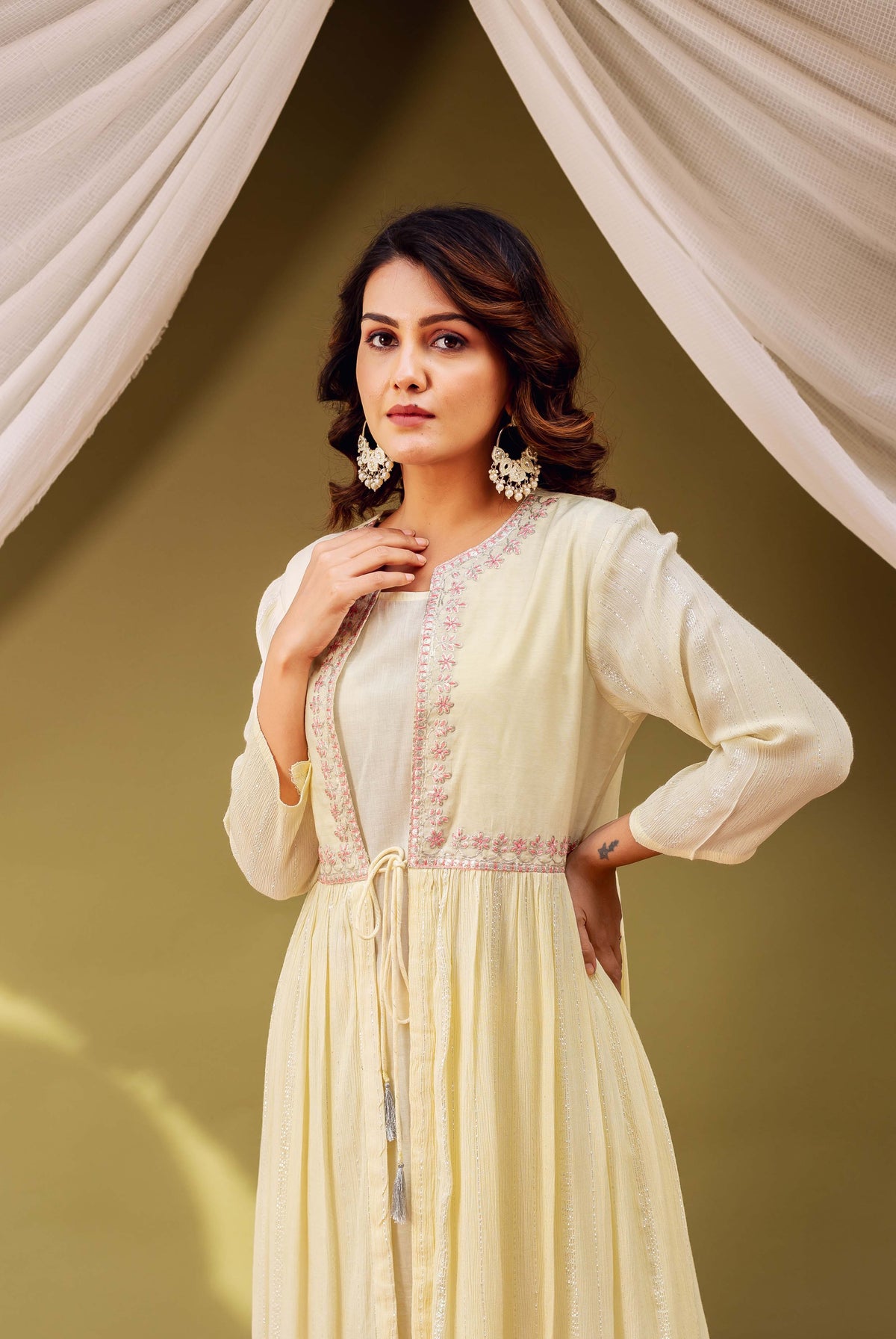Woman wearing a light yellow jacket-style kurta featuring pink embroidery, shimmer stripes, and tie-front.