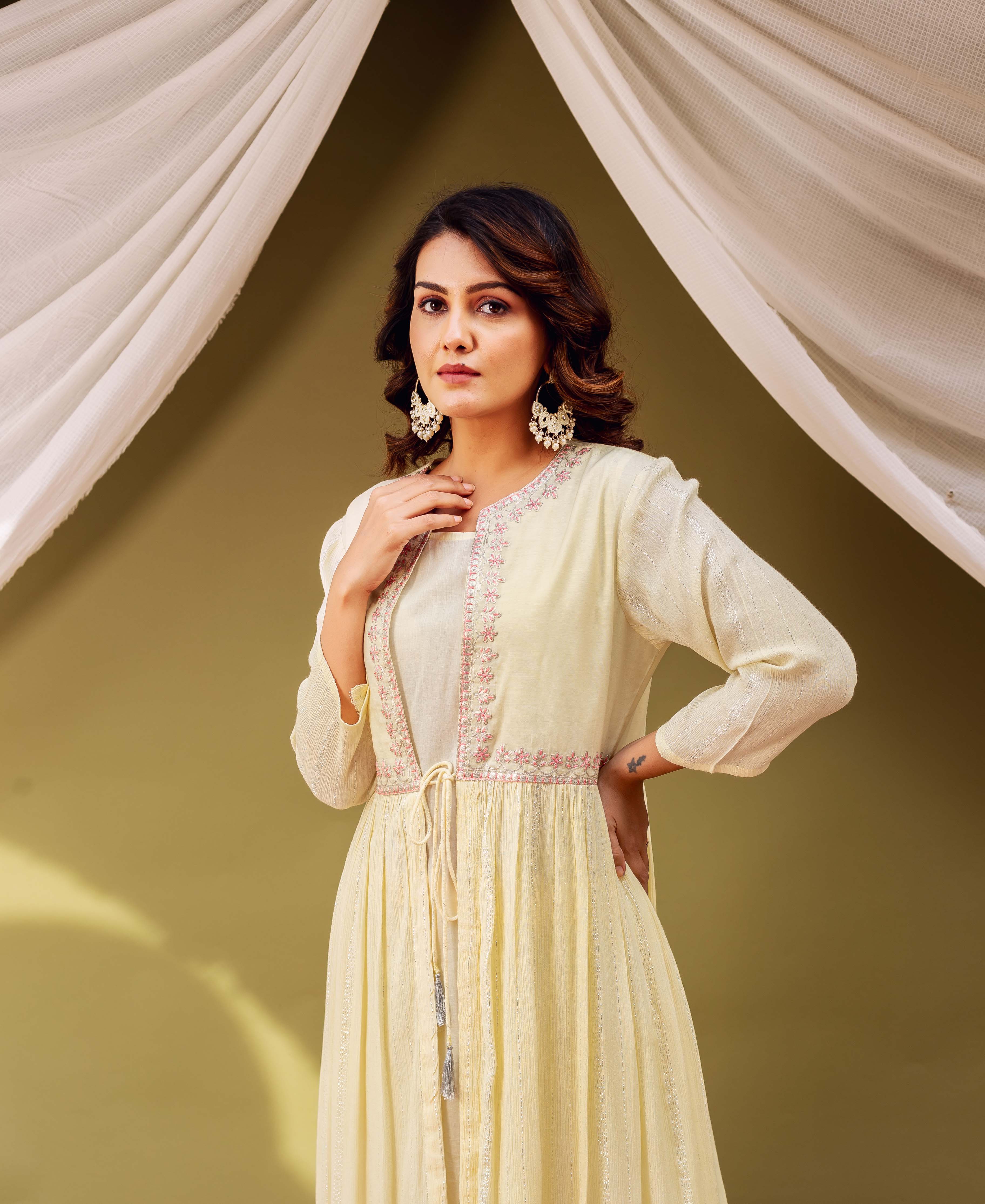 Woman wearing a light yellow jacket-style kurta featuring pink embroidery, shimmer stripes, and tie-front.