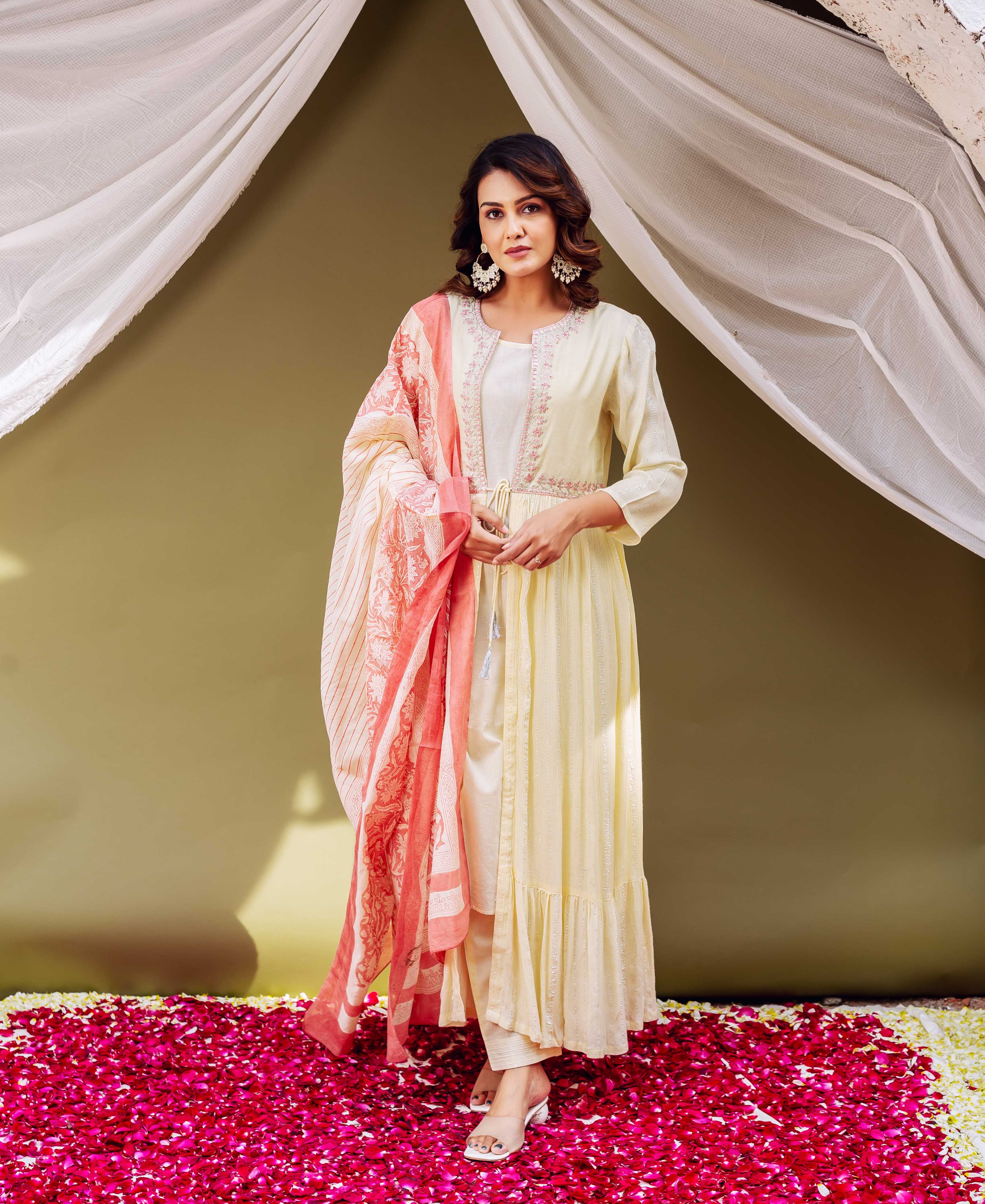 Woman in cream kurta with embroidered waist and pink and white shawl standing on flower petals.