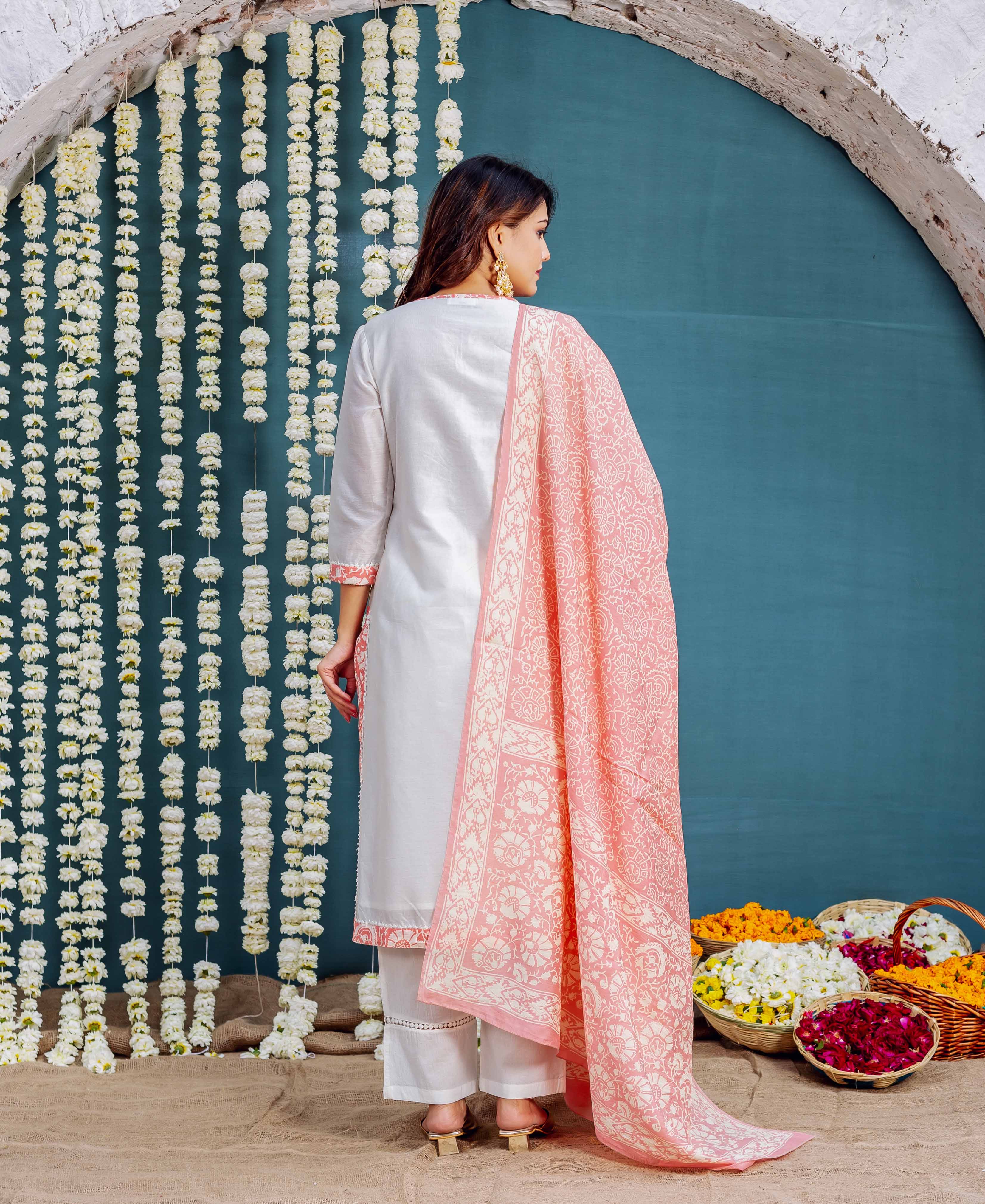 Side-back view of woman in white kurta set with a large pink block-printed dupatta.