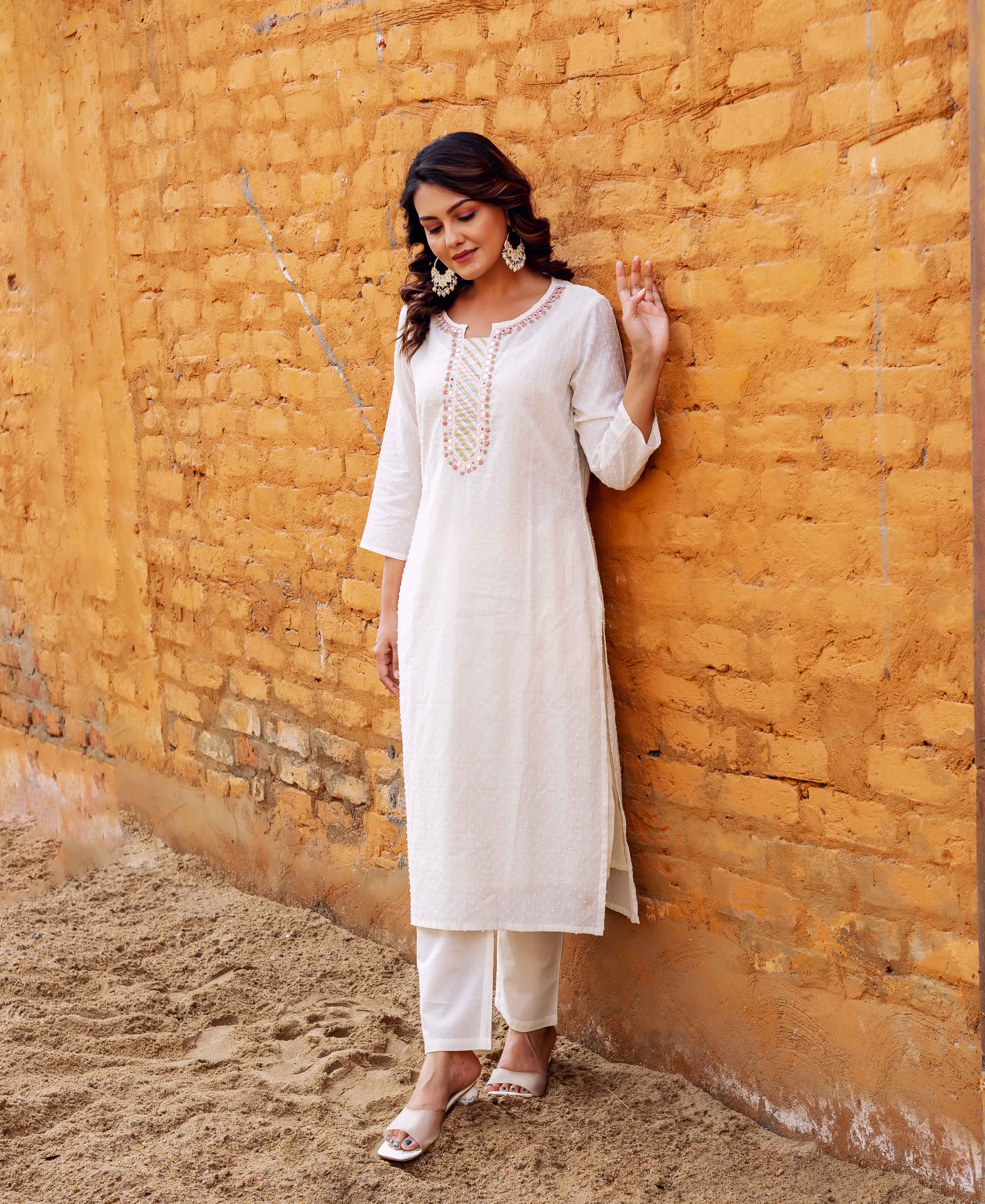A woman in a white kurta with a block-printed design on the front, standing against a brick wall.