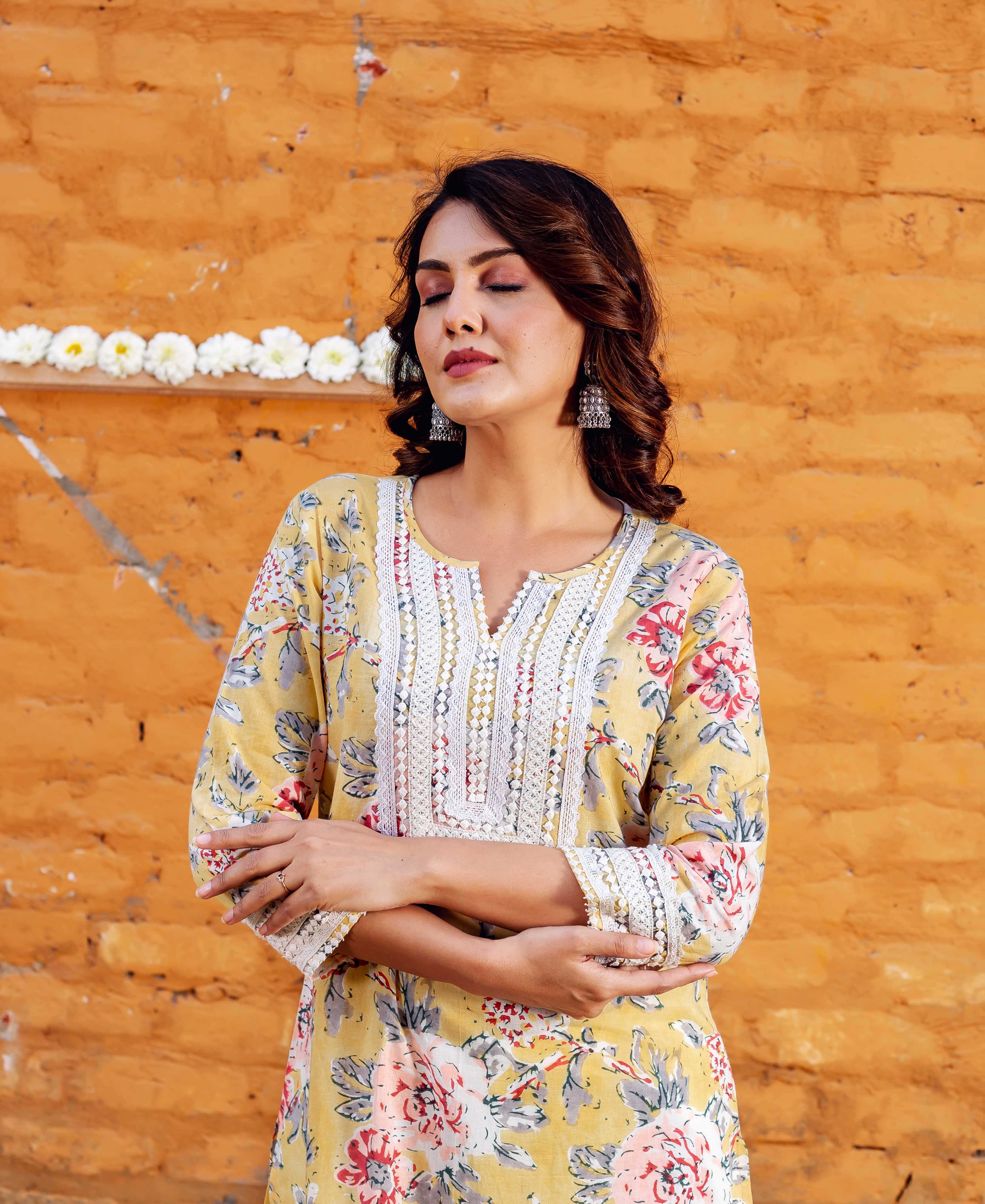 Woman wears yellow floral block printed kurta; white lace trim; pink, red, blue and grey flowers.