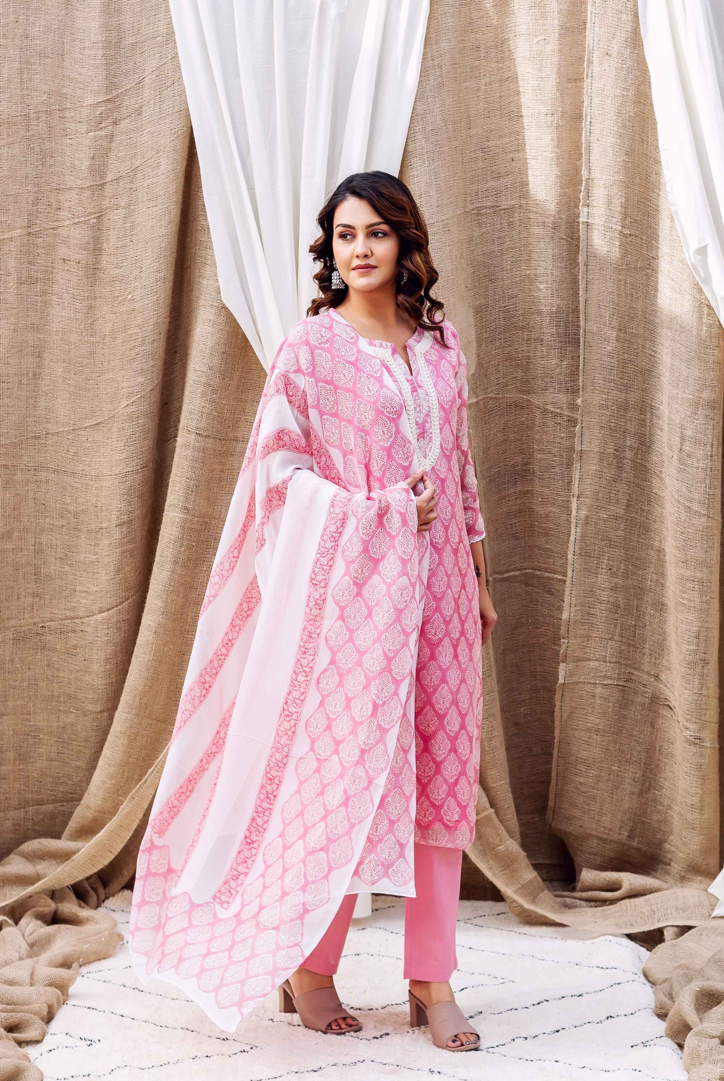 Woman models blush pink hand-block printed organza kurta, matching pants, and patterned dupatta.