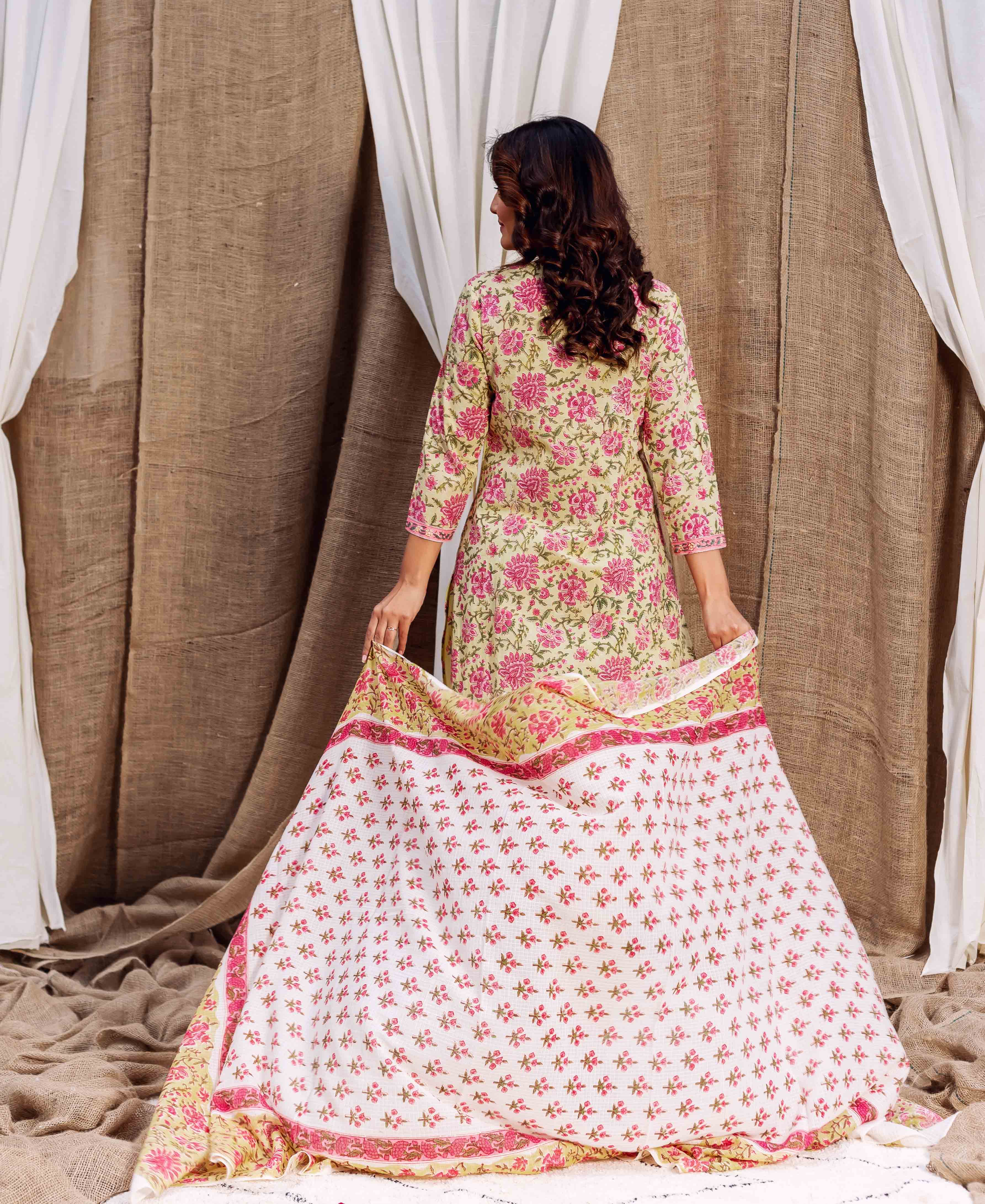 A woman in a floral dress holds a white dupatta with pink flowers.