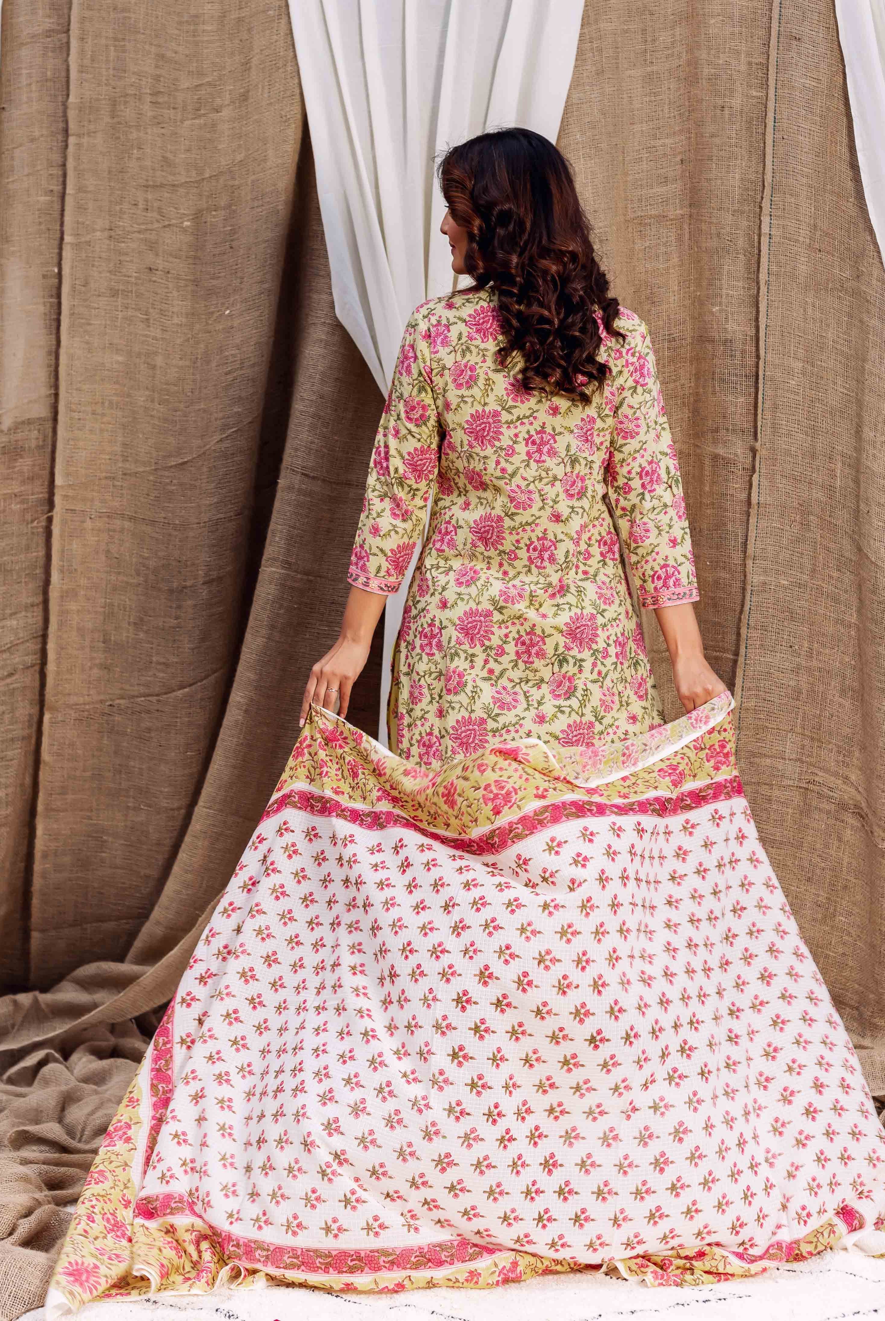 Woman, back to viewer, wears pale green kurta with pink florals, holding white printed fabric.