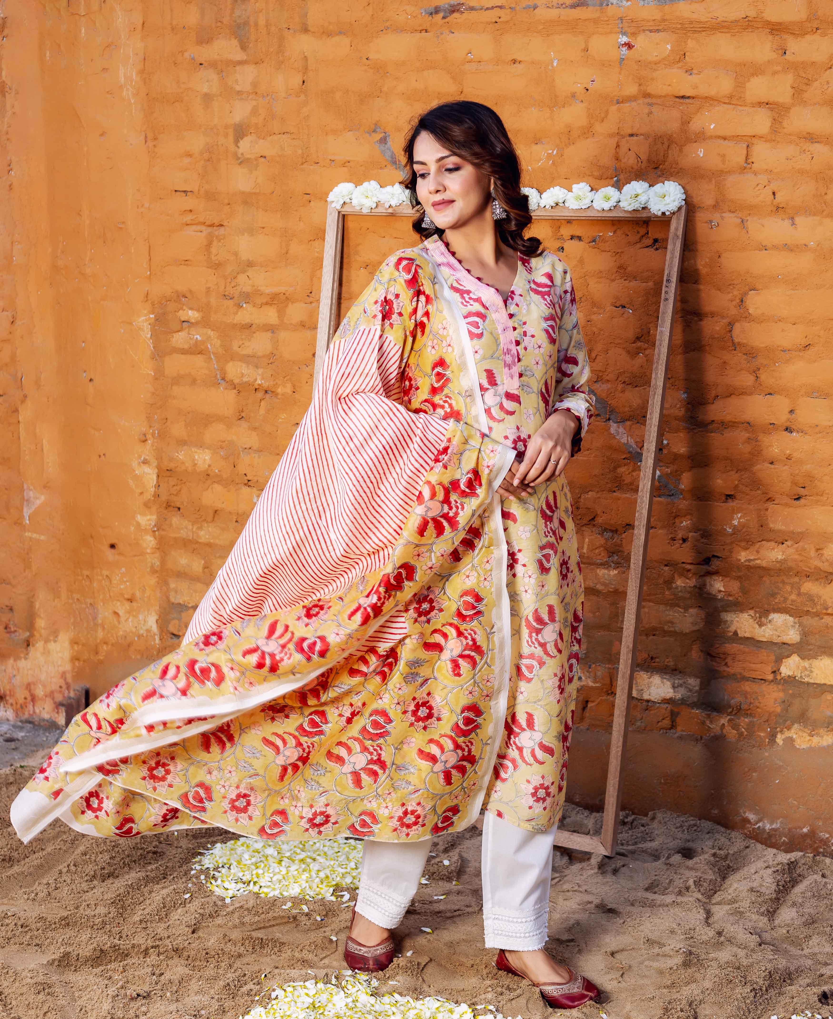 Model wears a yellow-red floral hand-block printed kurta set with a flowing striped dupatta.