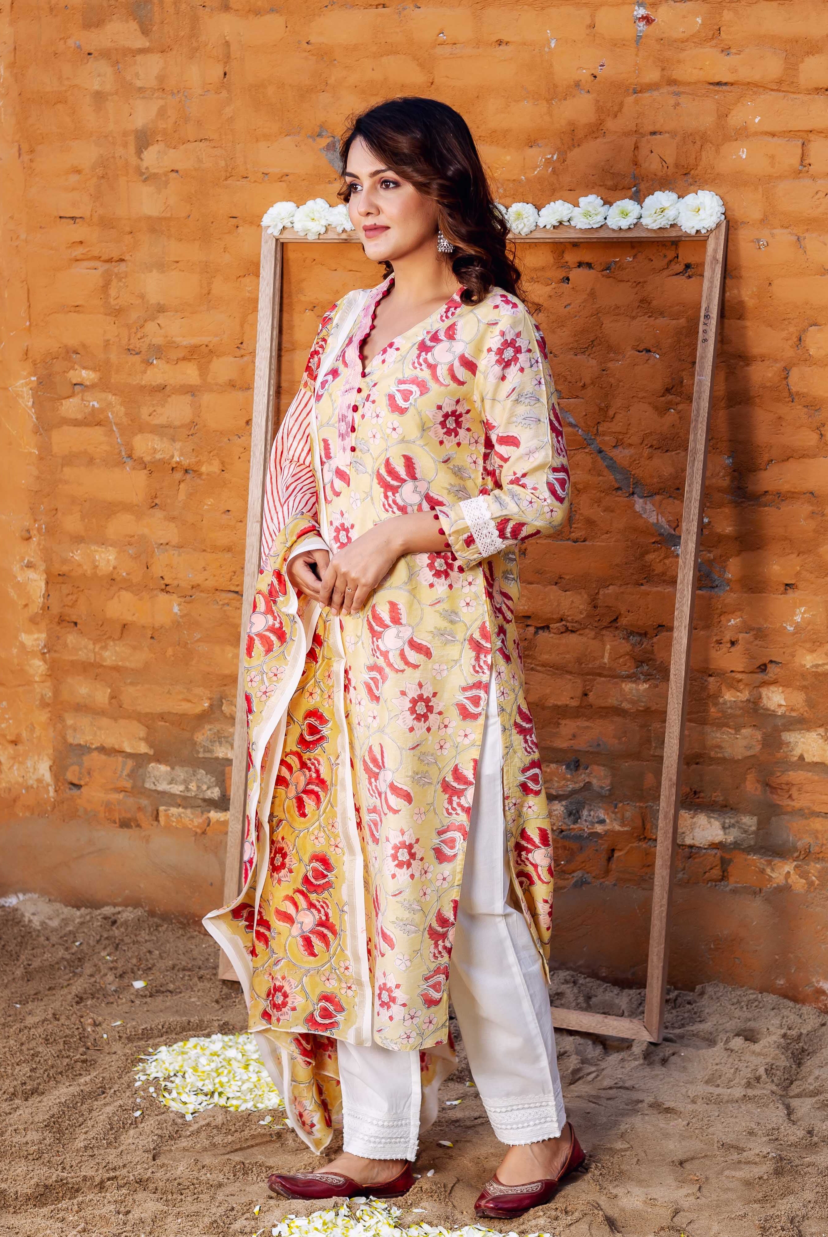 Standing model wearing yellow and red floral hand-block printed kurta set with dupatta.