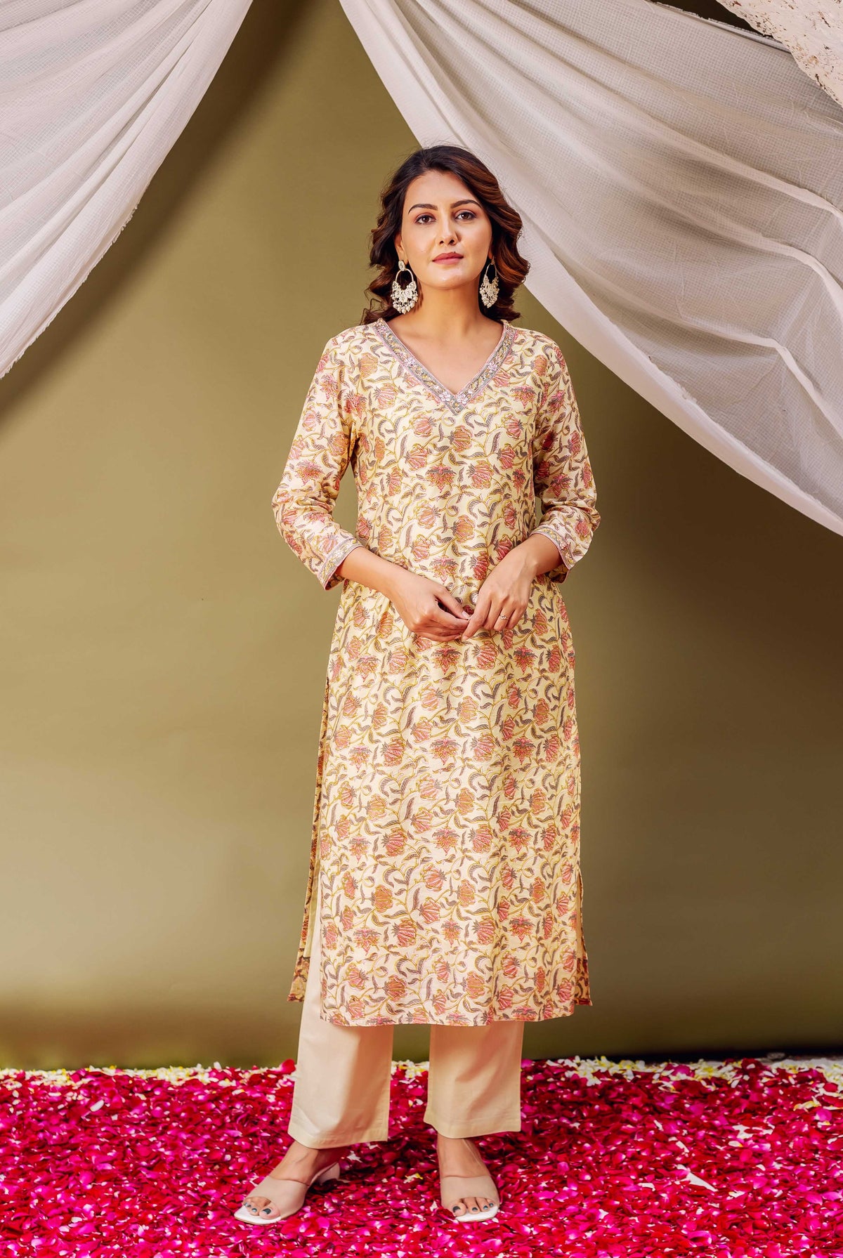 A woman in a green floral block print kurta with white pants and earrings.