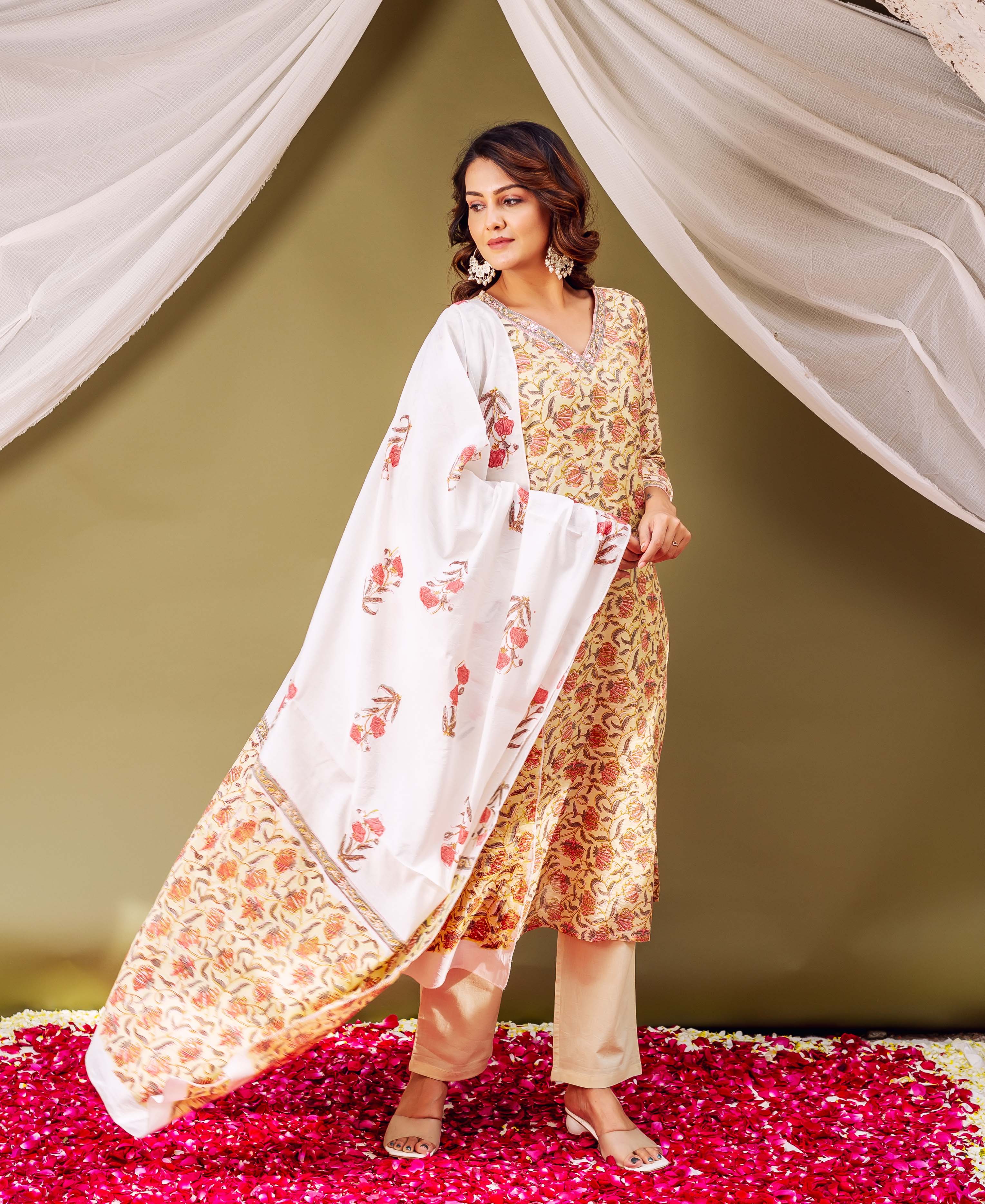 A woman in a yellow floral print kurta and white dupatta with pink flowers.