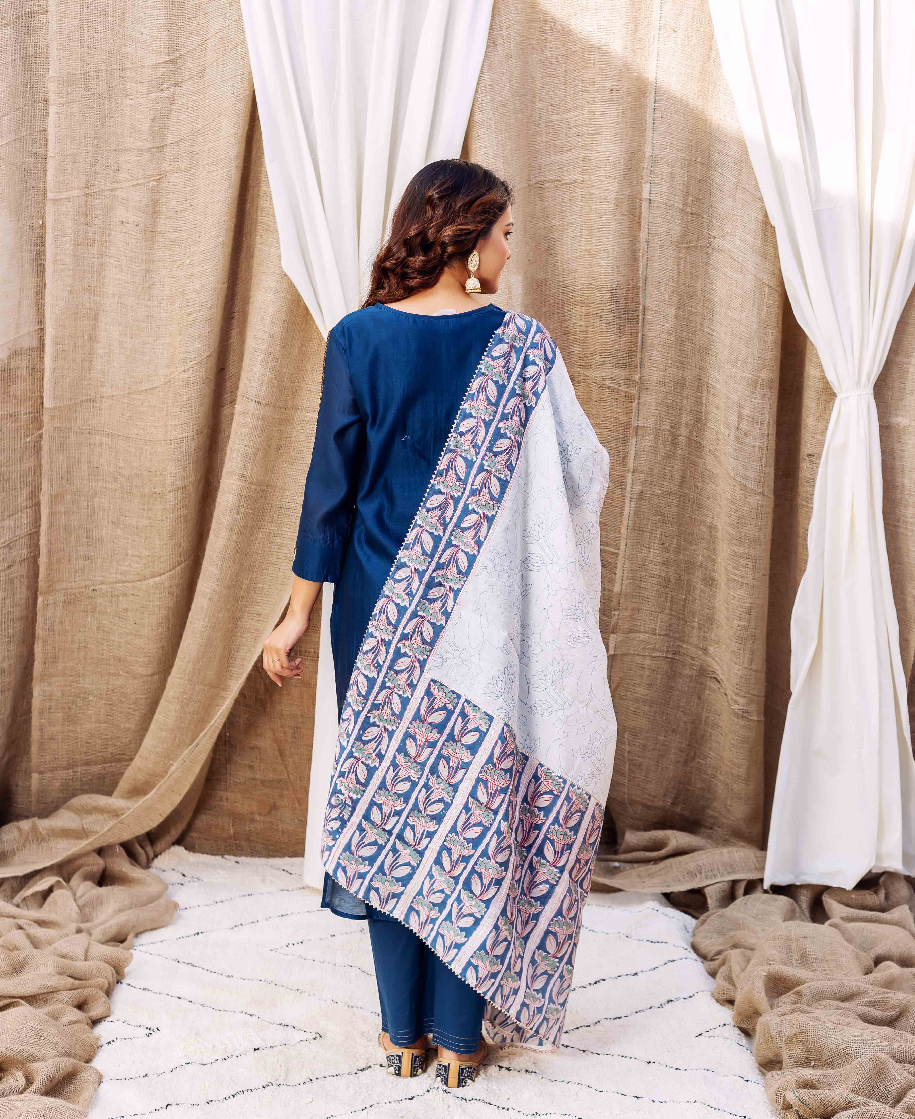 Back view of a woman in blue, with a white dupatta featuring blue and pink floral print.