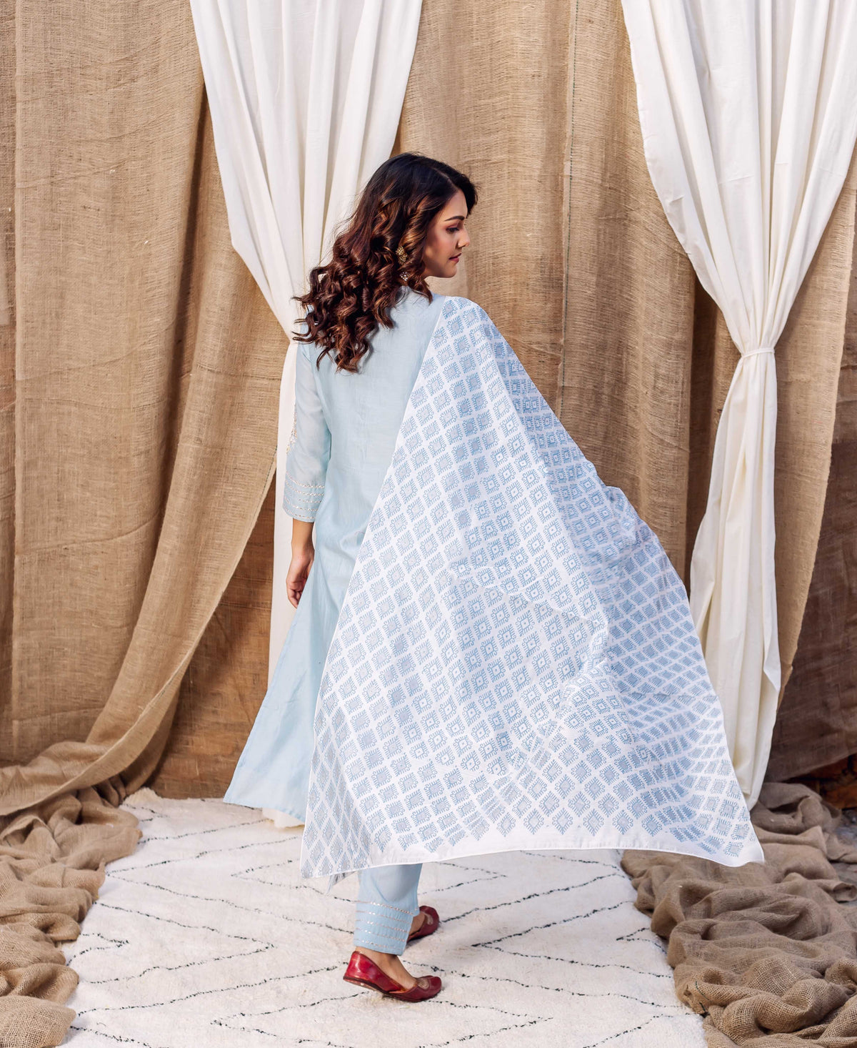 Back of model in azure kurta set with a flowing white hand-block printed geometric dupatta.