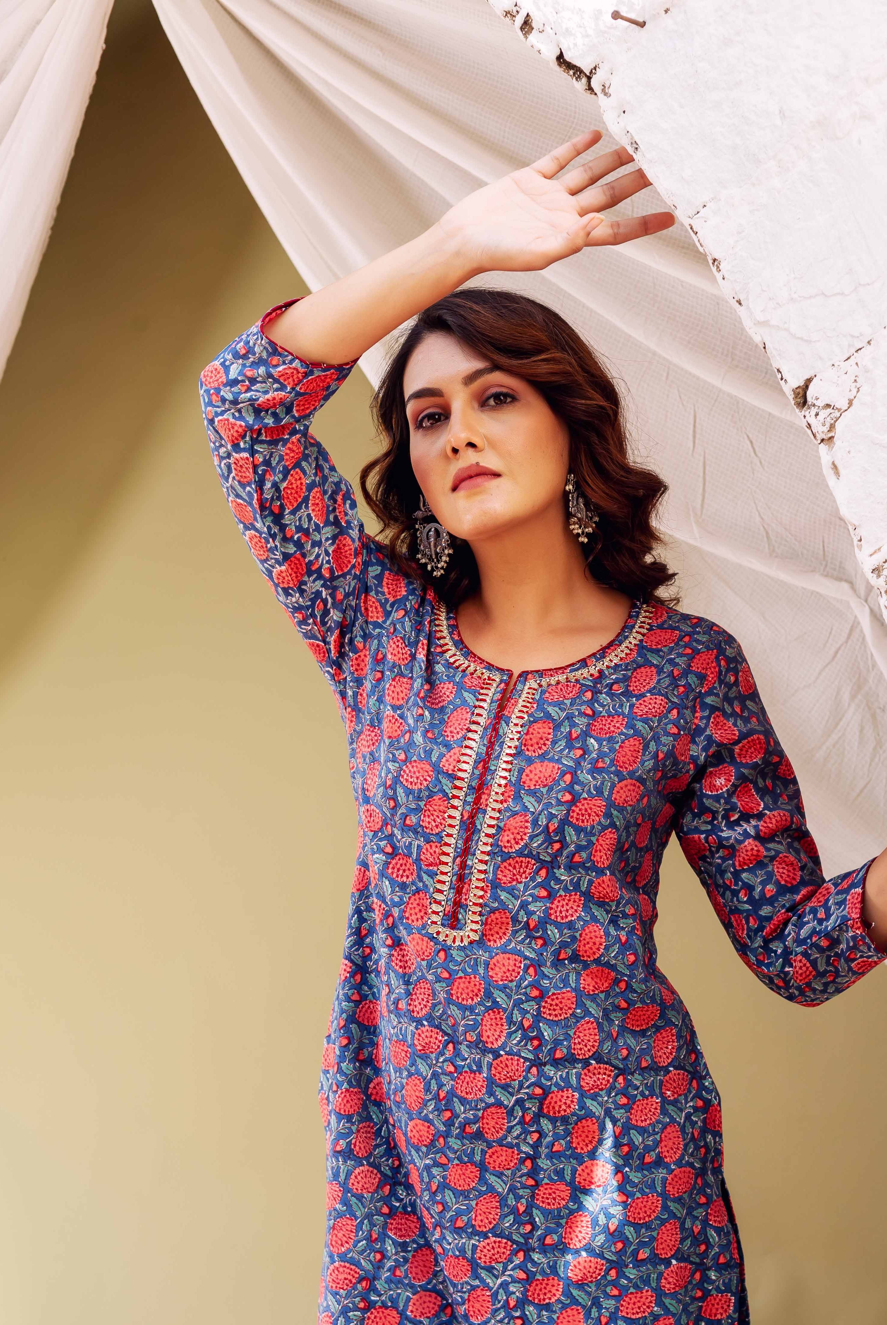 Woman in blue kurta with red floral print and gold trim.