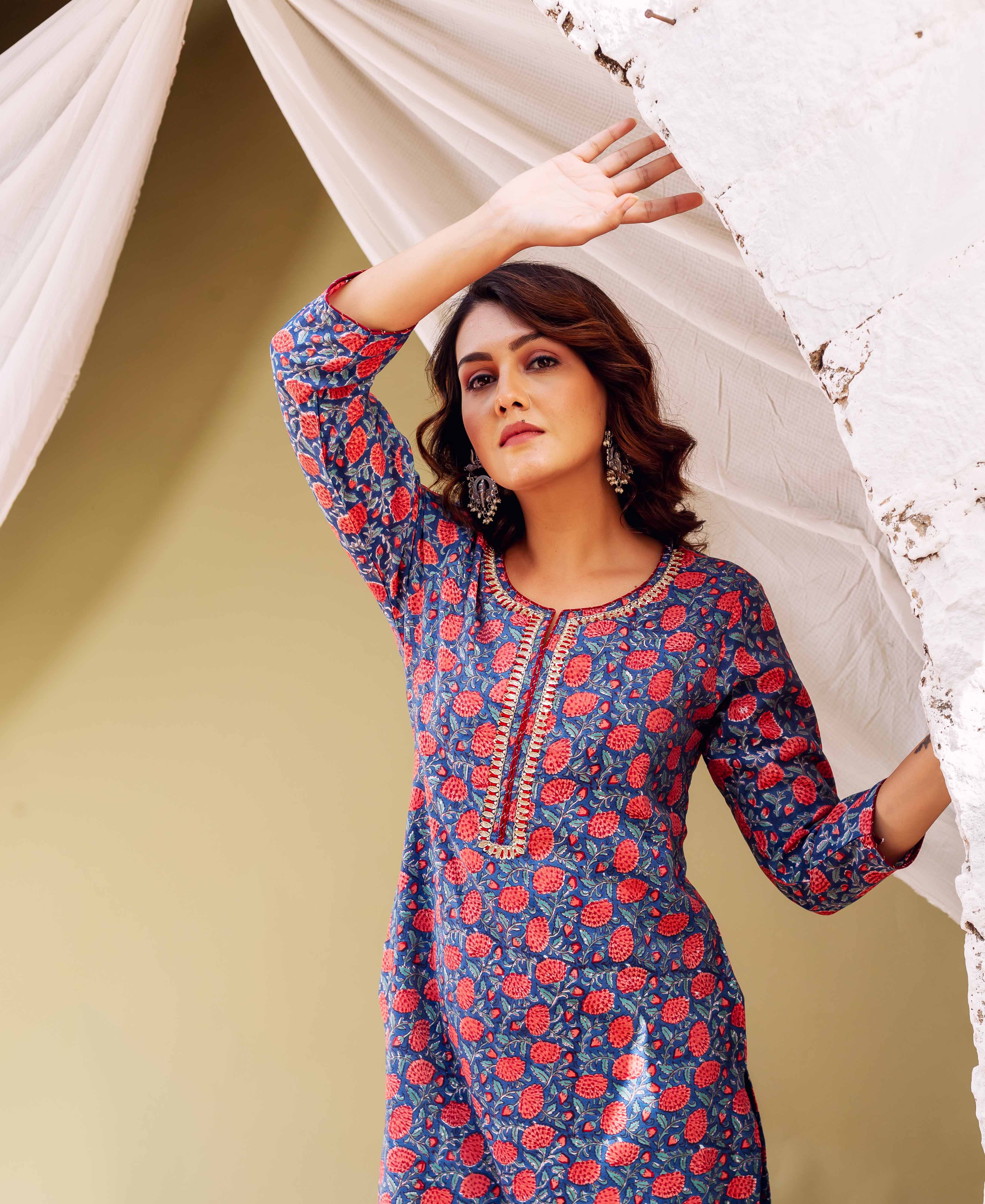 Woman in blue kurta with red floral print and gold trim.