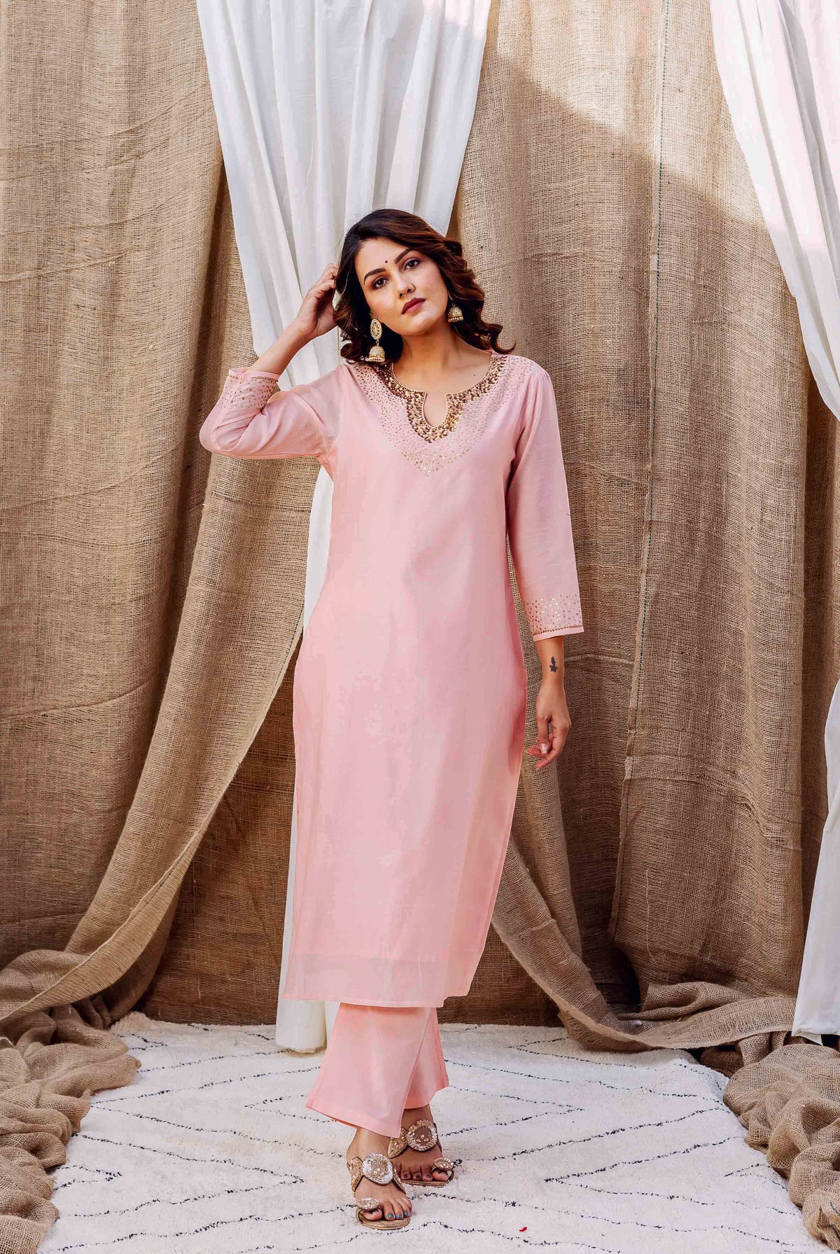 Full-length shot of standing model in soft pink kurta set with golden embellished V-neck and sleeves.