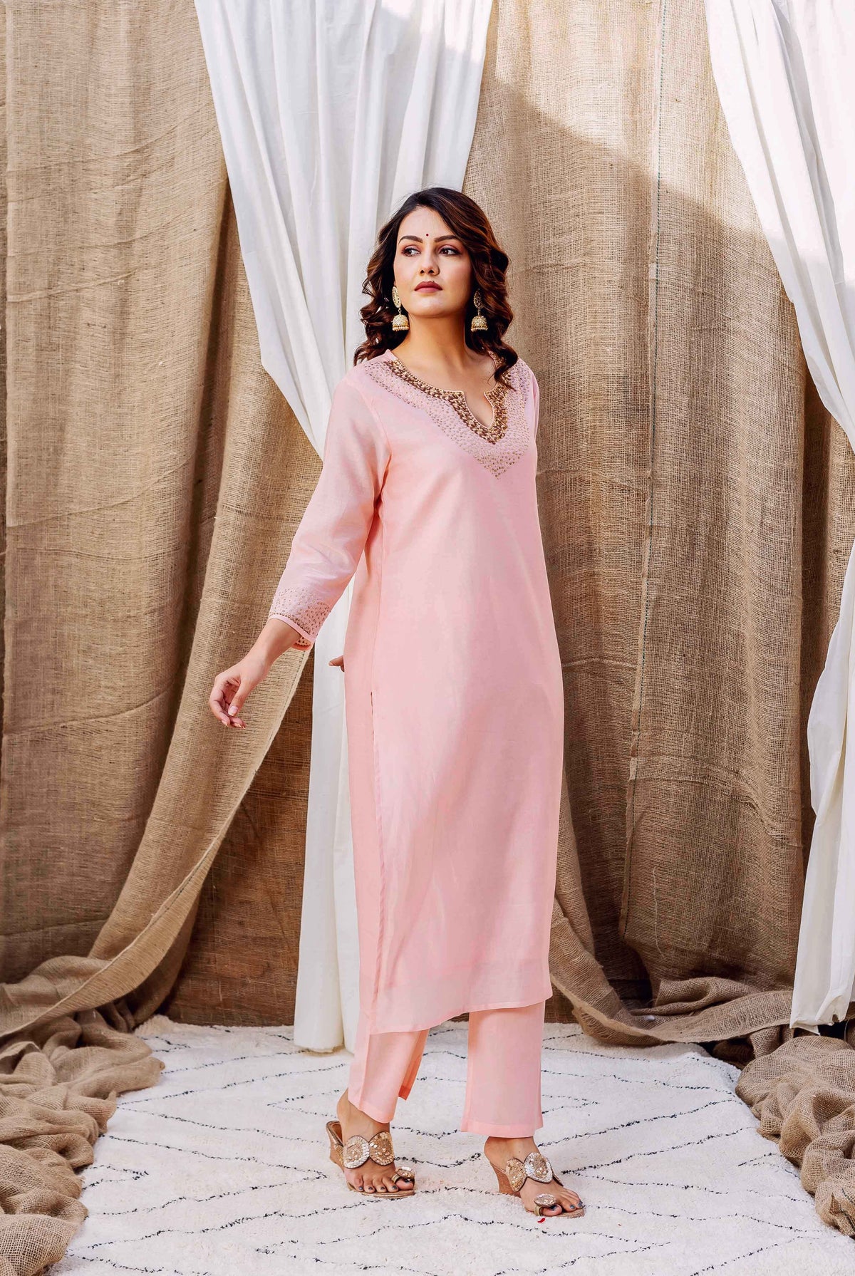 Model in a rose pink kurta set with intricate golden embroidered V-neckline and cuffs.