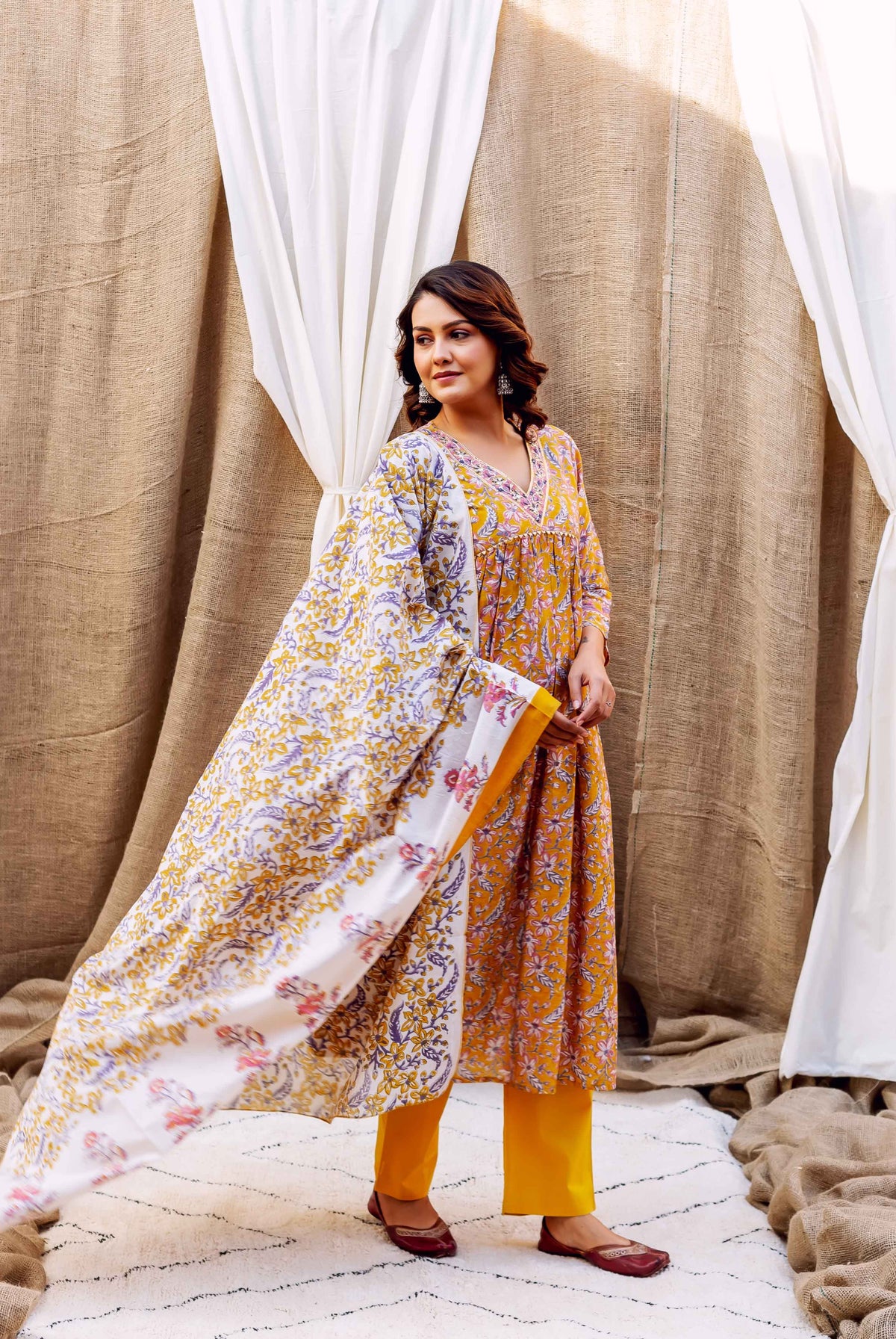 Woman in a golden spice block-printed kurta, pants, and flowing white floral dupatta.